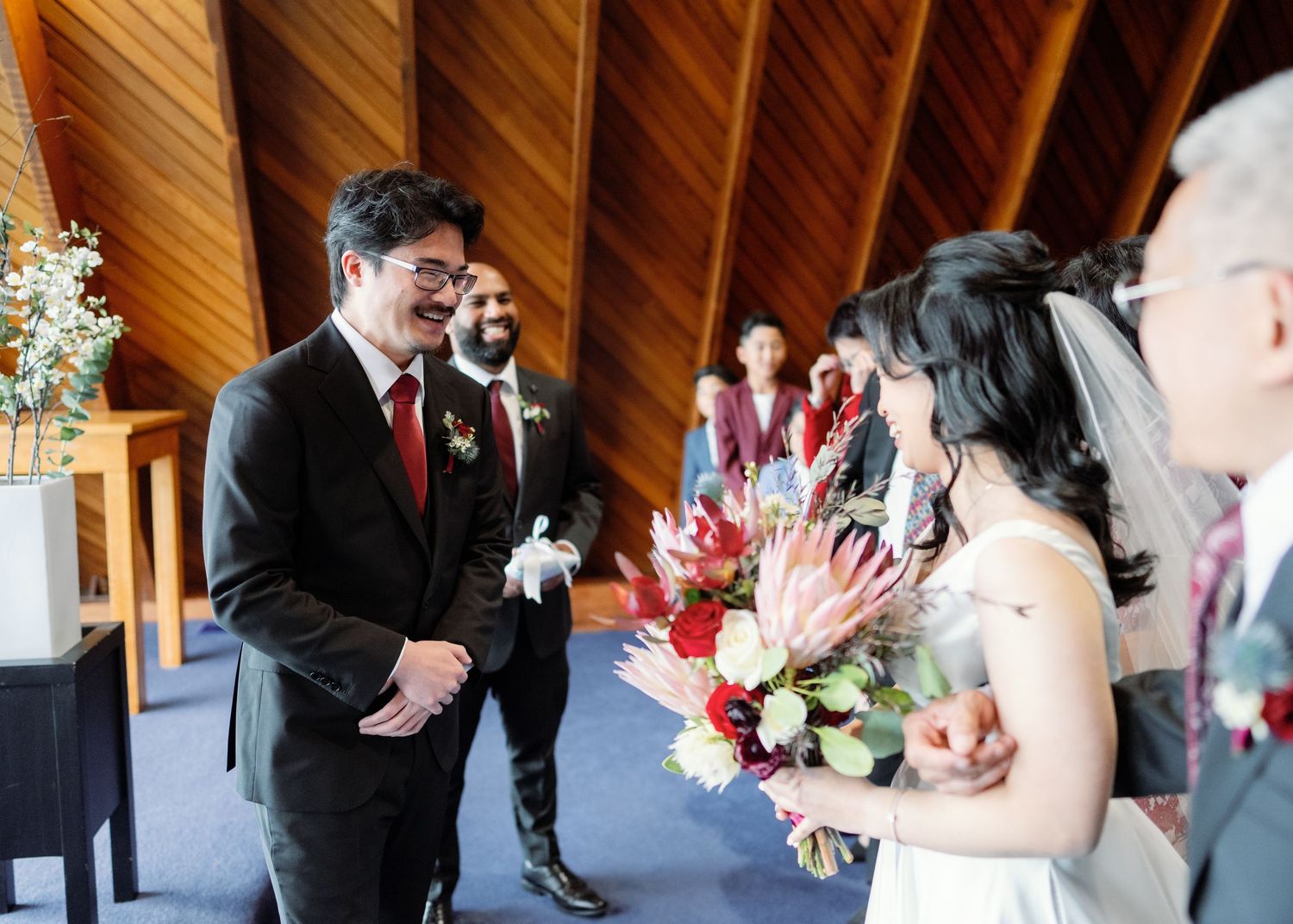 Joyful moment captured during indoor wedding ceremony with bright flowers and wooden beamed ceiling.