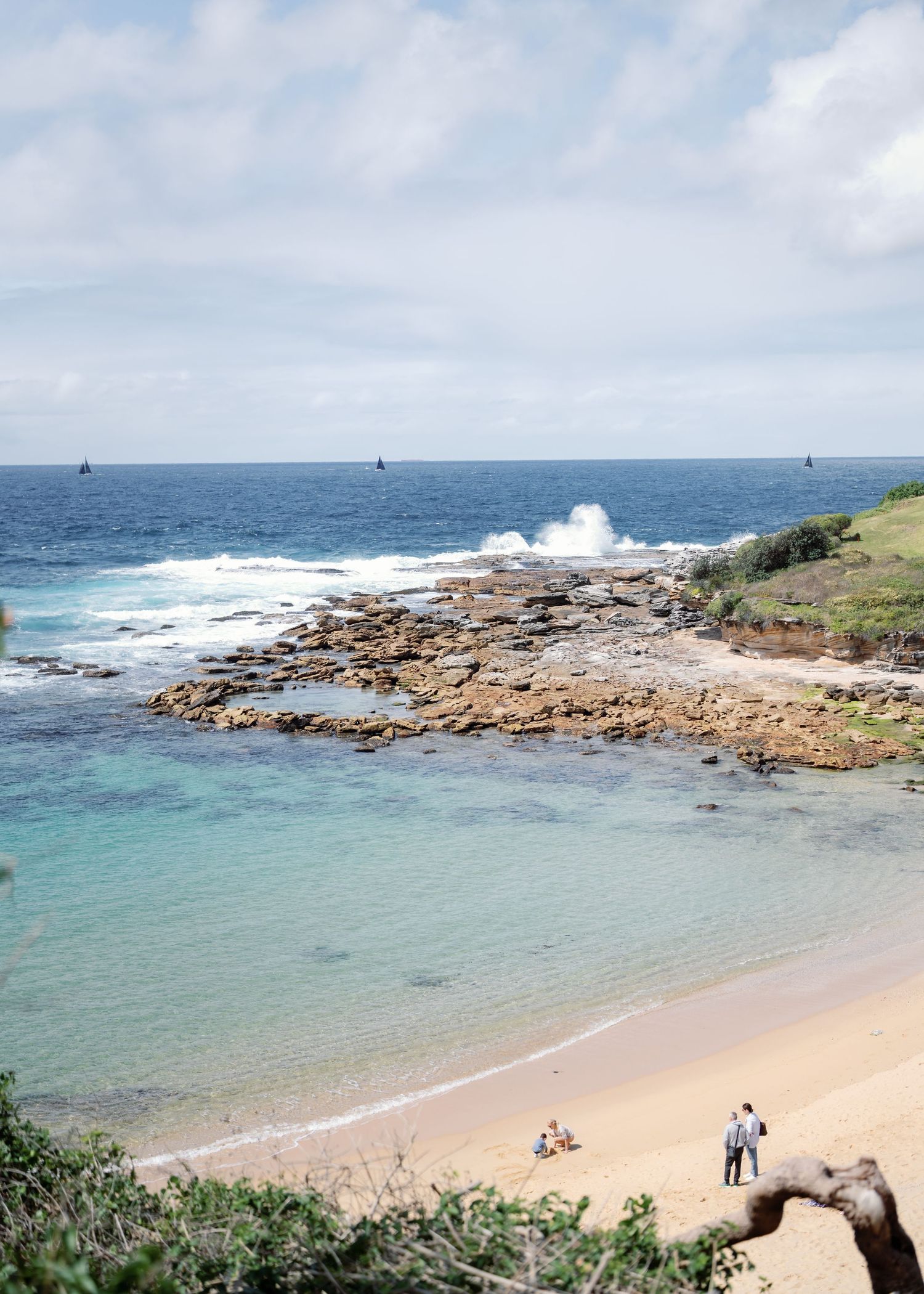 Rocky coastal beach landscape with turquoise waters and crashing waves against stone formations.