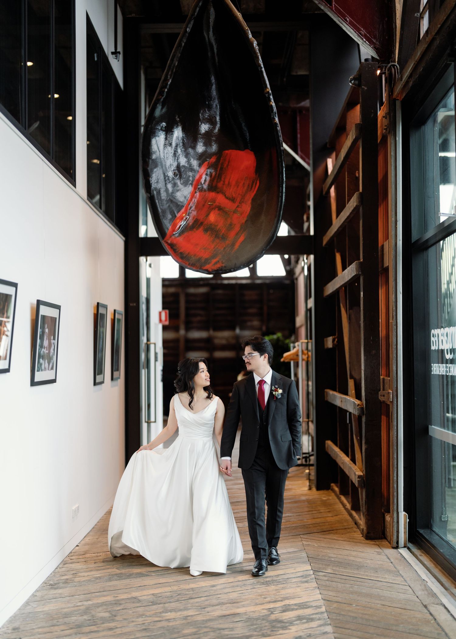 A couple walks down a rustic hallway with industrial decor and a large suspended boat.