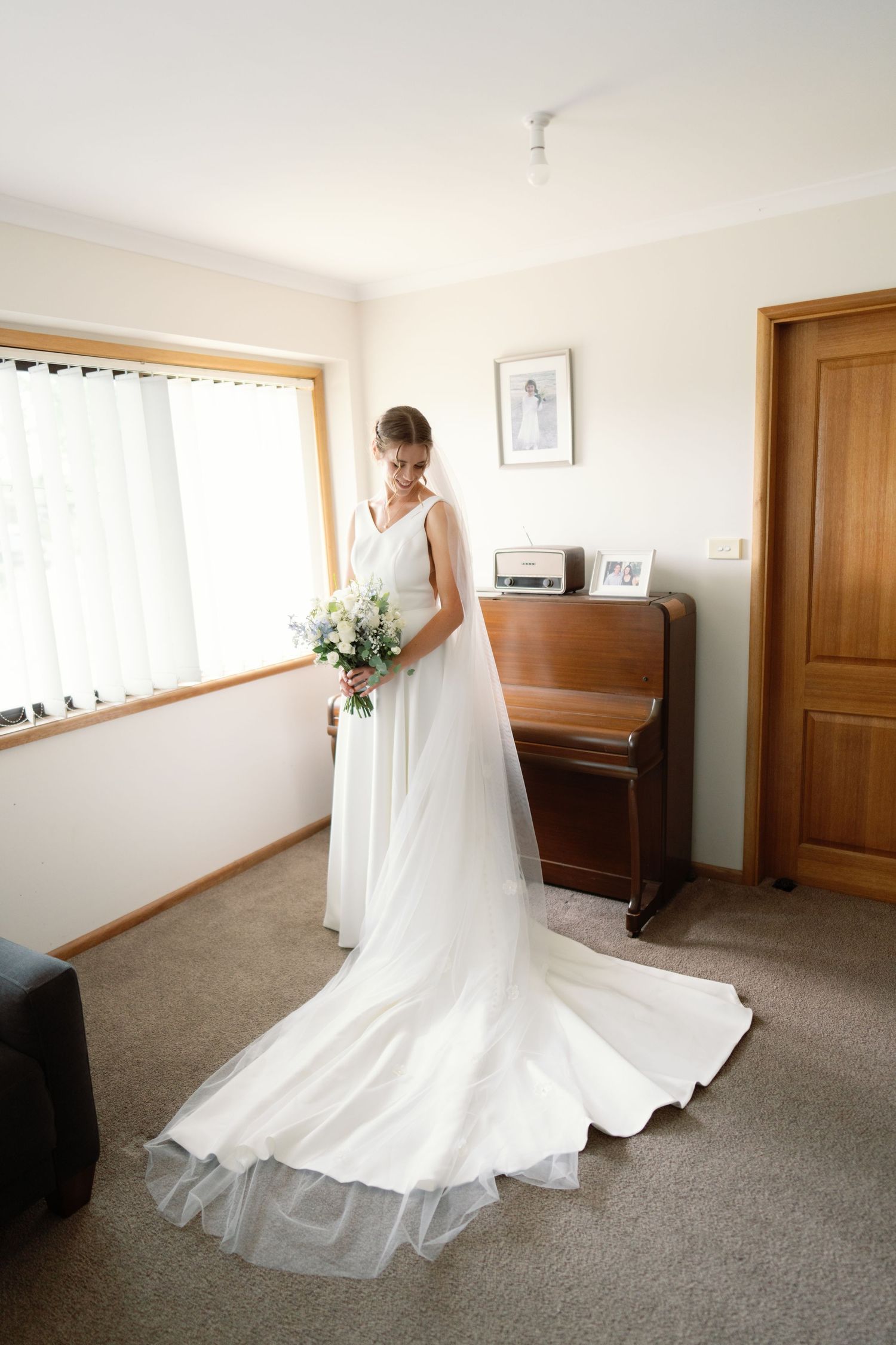 Wedding dress with flowing train photographed in a room with wooden doors and carpeted floor.