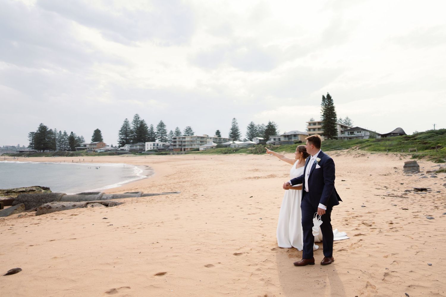 Couple walking along a peaceful beach shoreline on an overcast day.