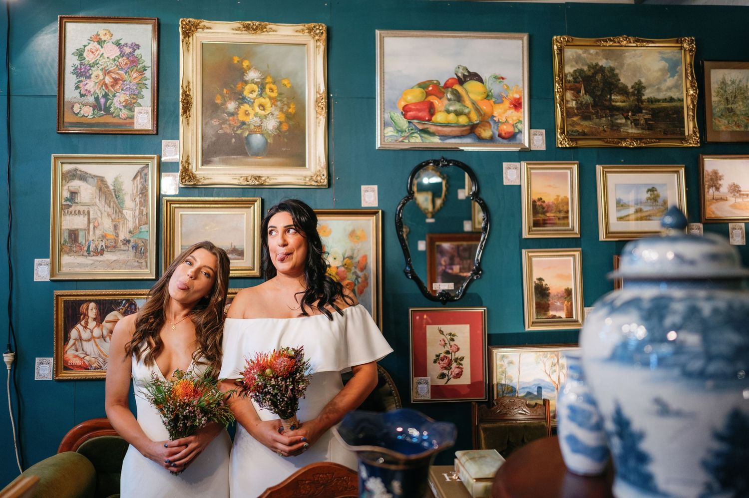 Art gallery wall with vintage frames displaying various paintings and artwork against a teal blue wall.
