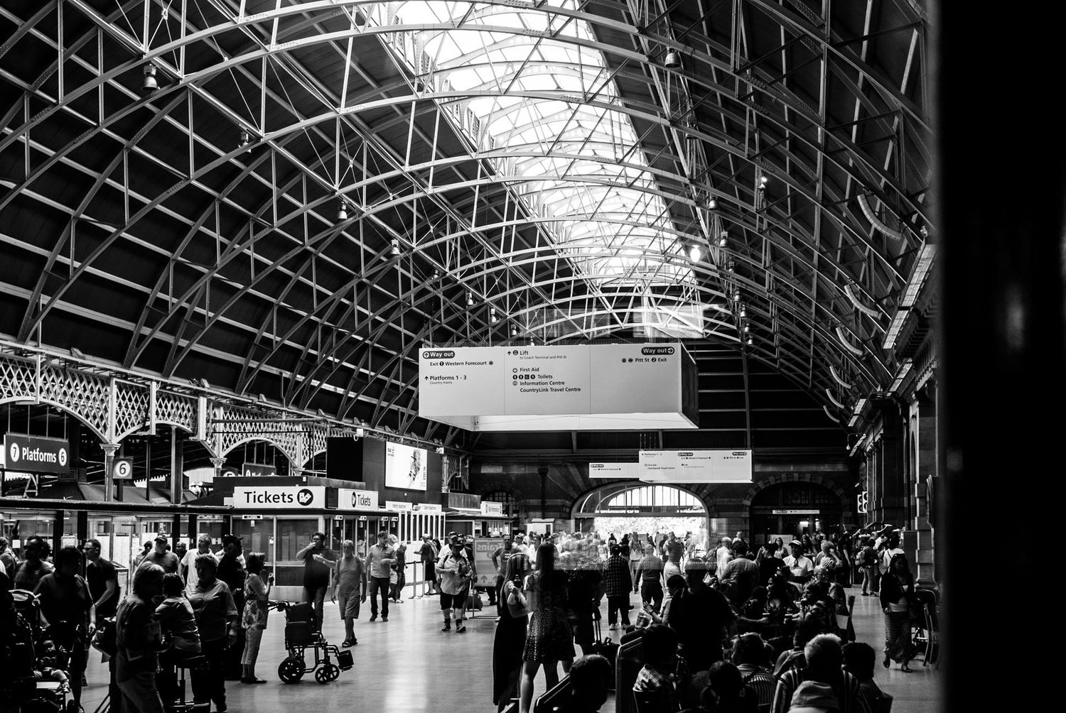 A black and white photograph of a busy train station concourse with arched ceiling.