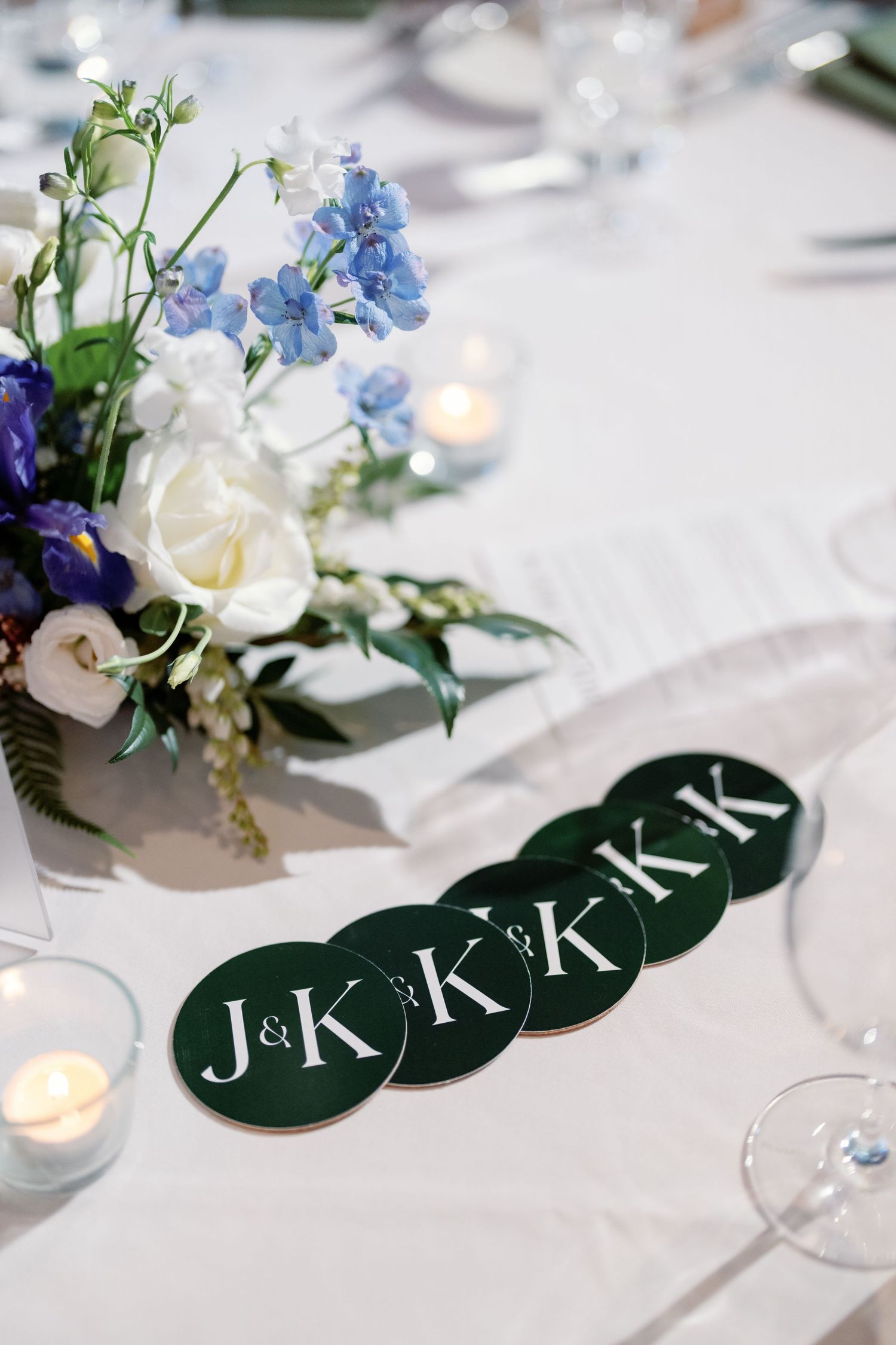 Green circular wedding coasters with J&K monogram beside floral centerpiece and candles.