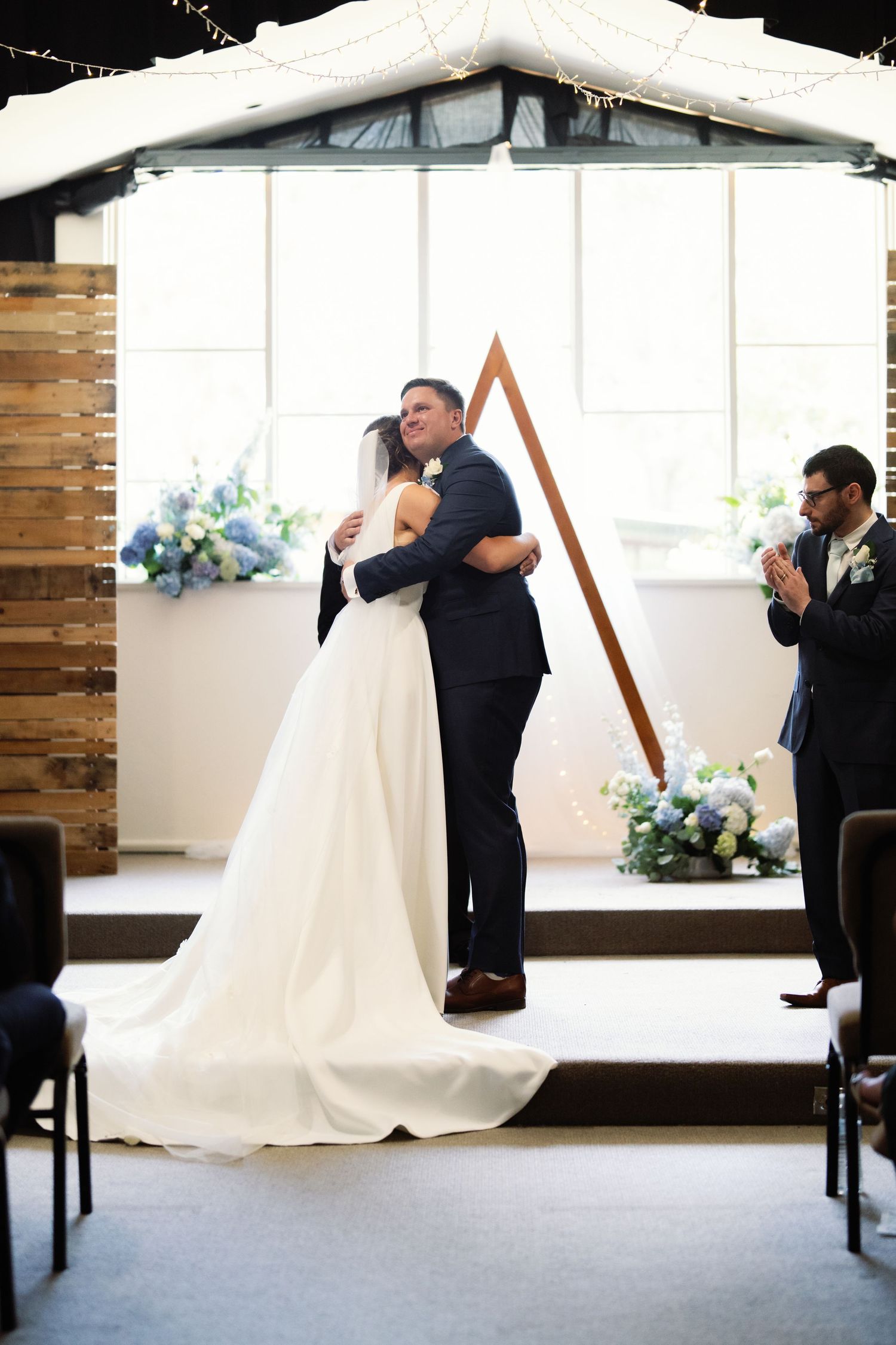 Indoor wedding ceremony setup with wooden accents and white drapery.