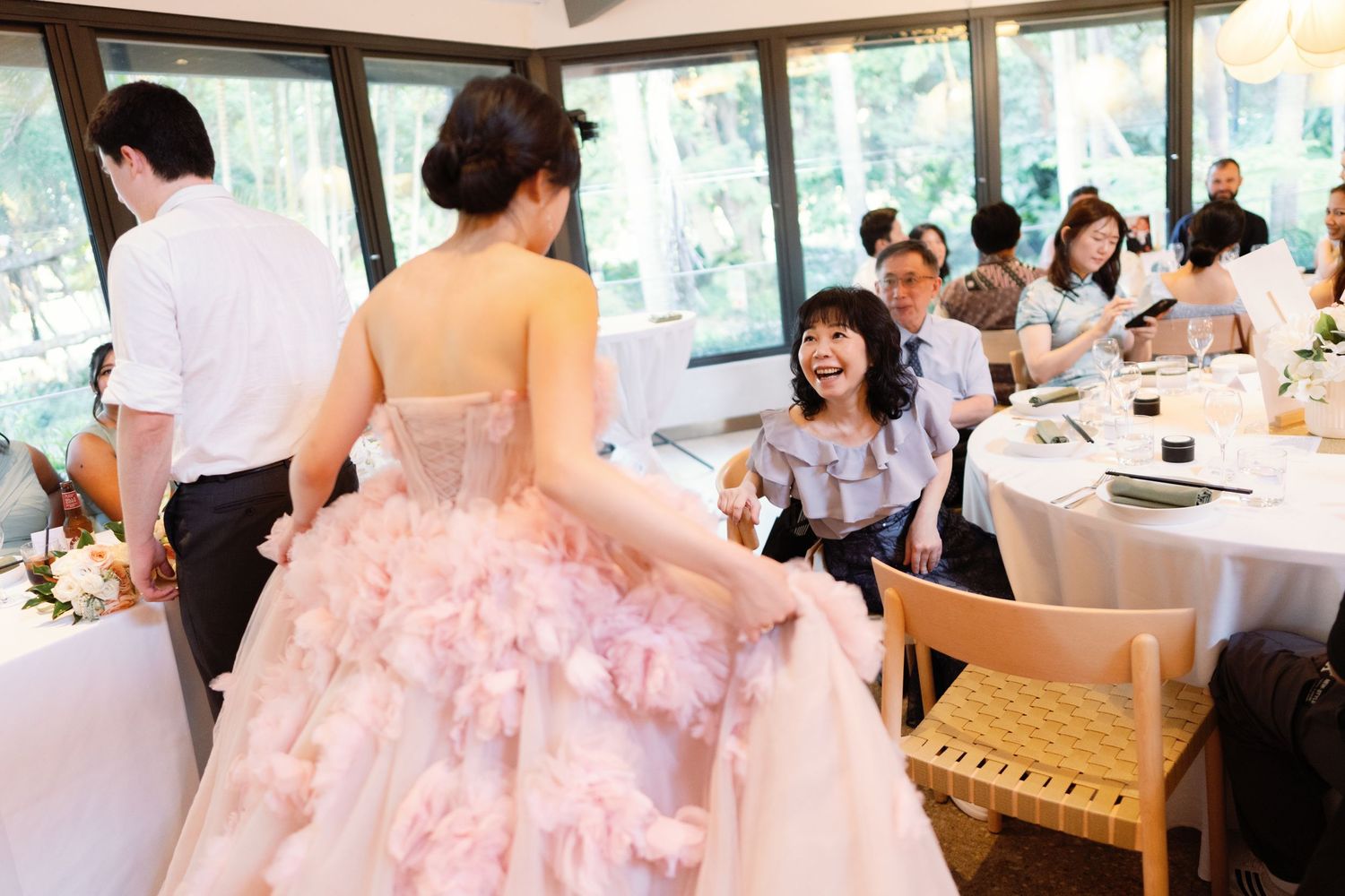 Wedding reception in bright windowed venue with guests seated at decorated tables.
