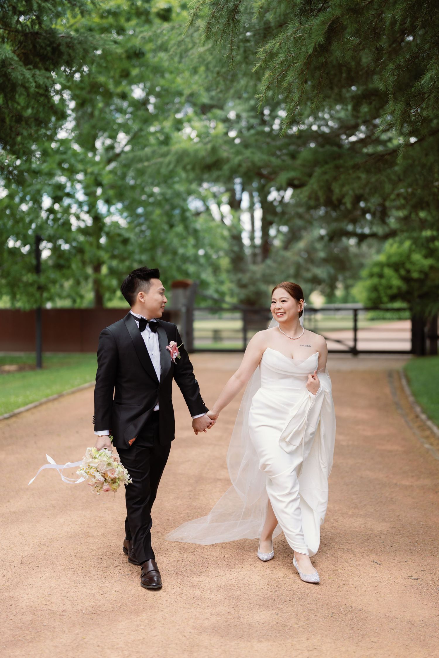 Playful wedding couple running and dancing together on a tree-lined path.