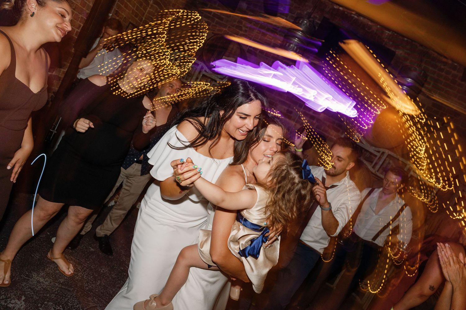 Dance party under warm string lights with festive atmosphere in rustic venue.