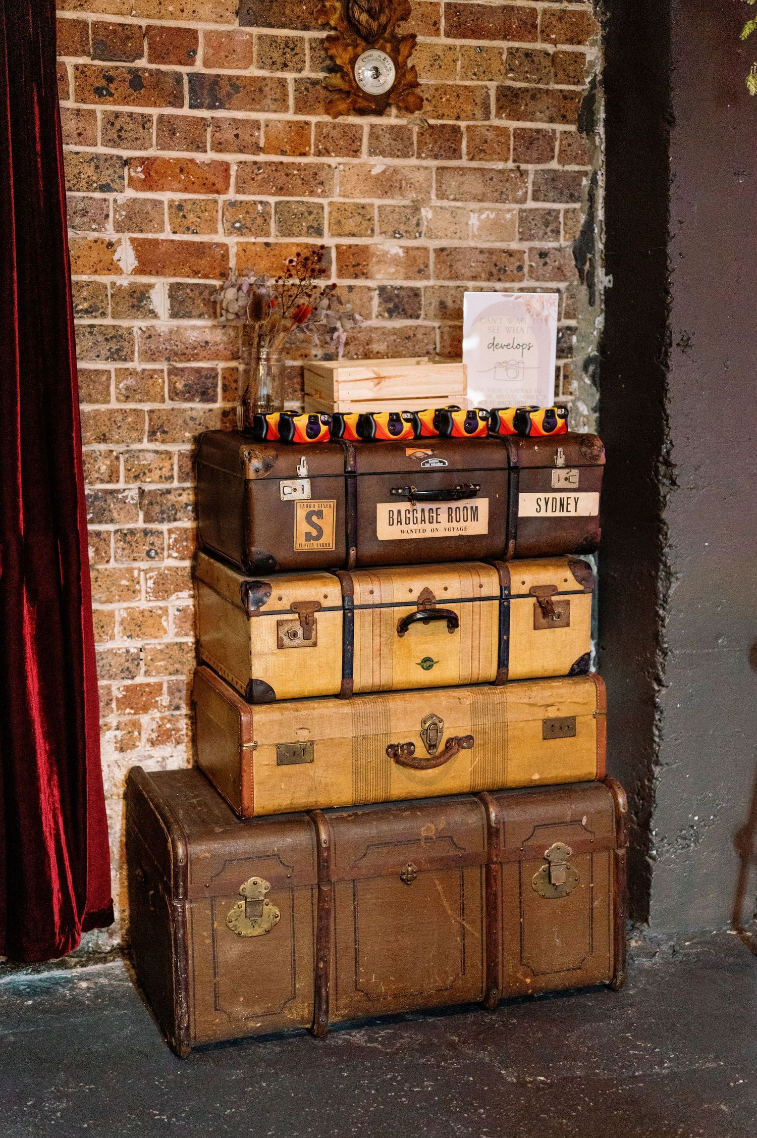 Antique travel trunks and suitcases arranged against rustic brick wall in dimly lit space.