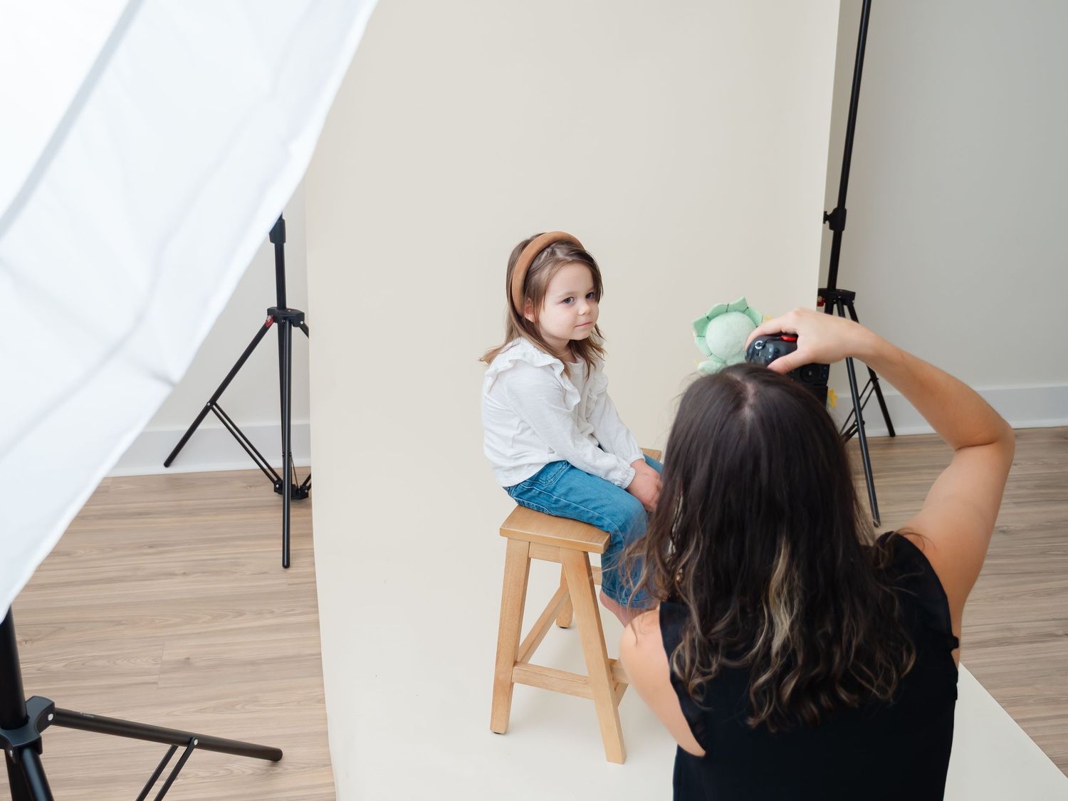 Photographer adjusts camera lighting and tripod settings in a bright minimal photography studio setup.