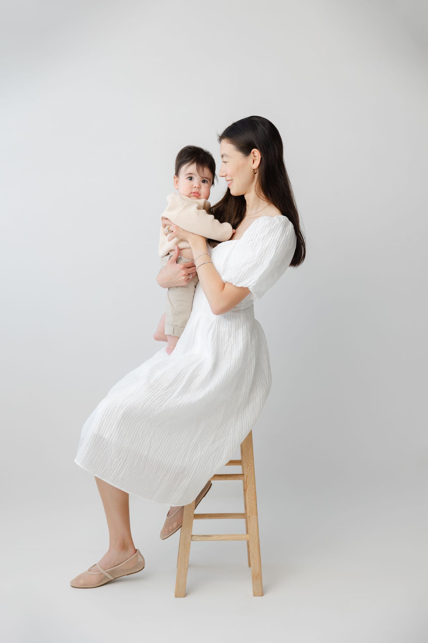 A tender moment captured in white dresses against a light backdrop, showing gentle interaction and connection.