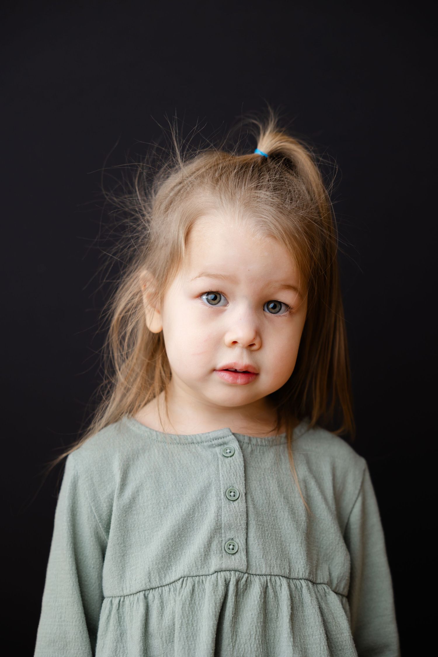 A sequence of portrait photos showing a small child in a sage green dress against a dark background.
