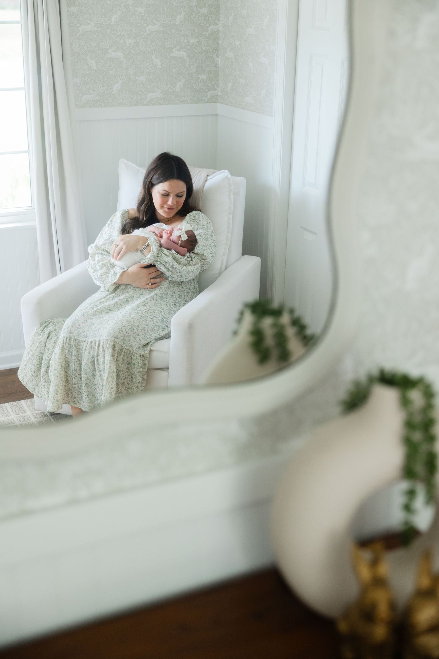 A person in a white lace dress rests peacefully on an elegant chaise lounge near a bright window.