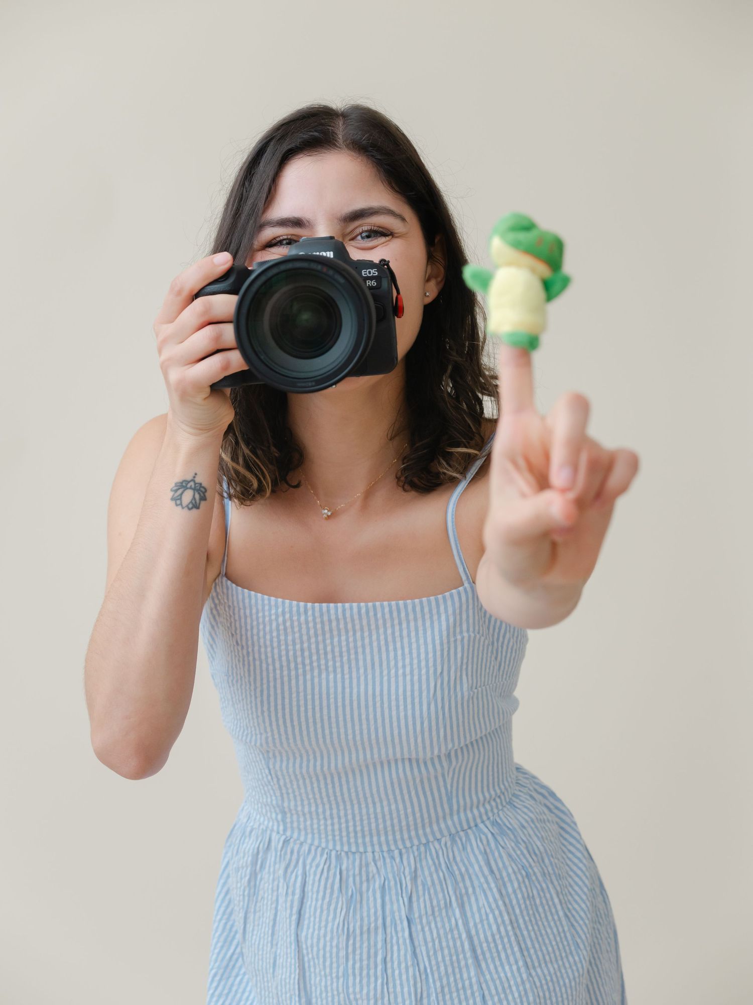Person holding green props while taking photos with professional camera in light blue summer dress.
