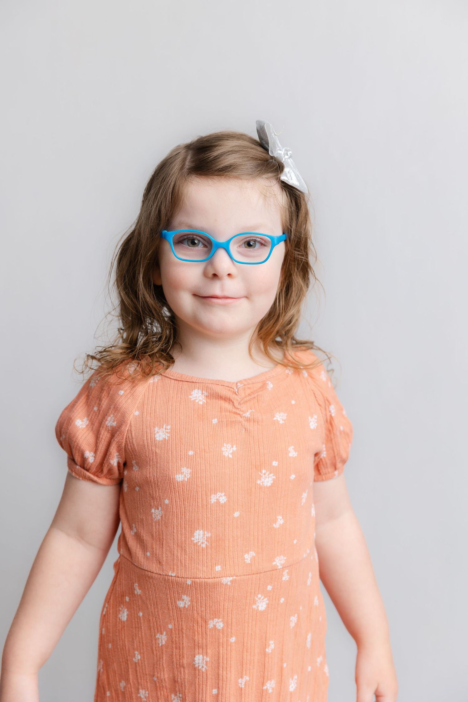 A child wearing a peach floral dress and blue glasses poses with expressions across four connected photos.