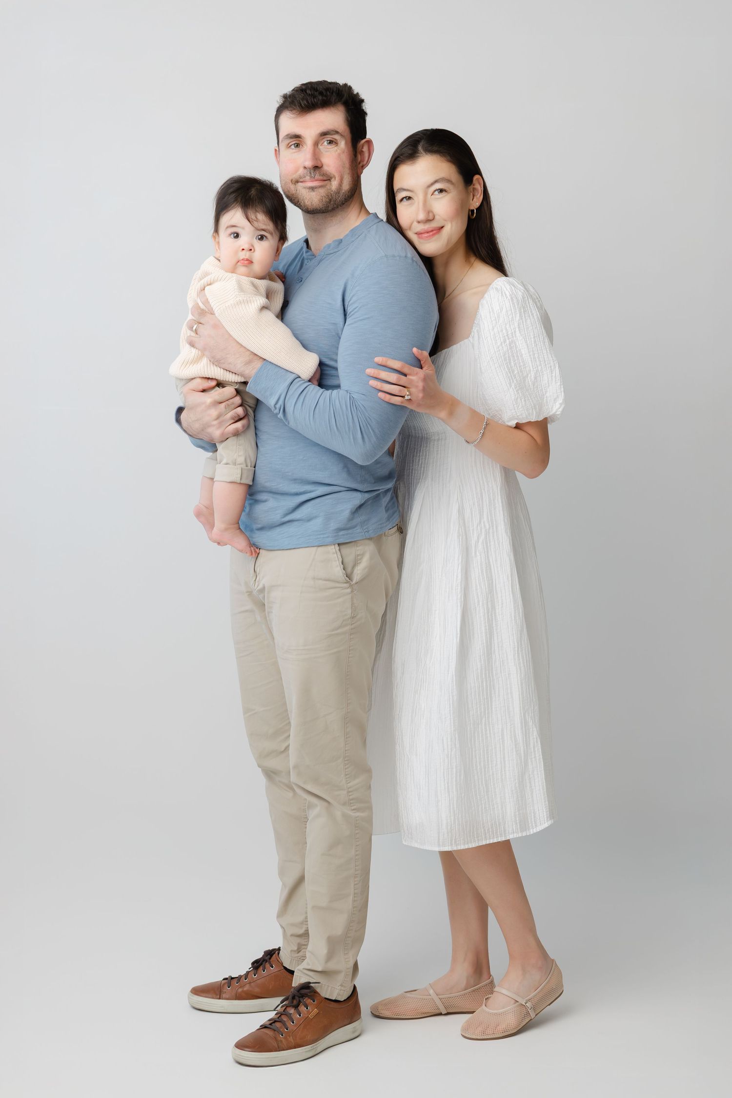 A family in coordinated blue and white outfits poses together against a light gray studio backdrop.