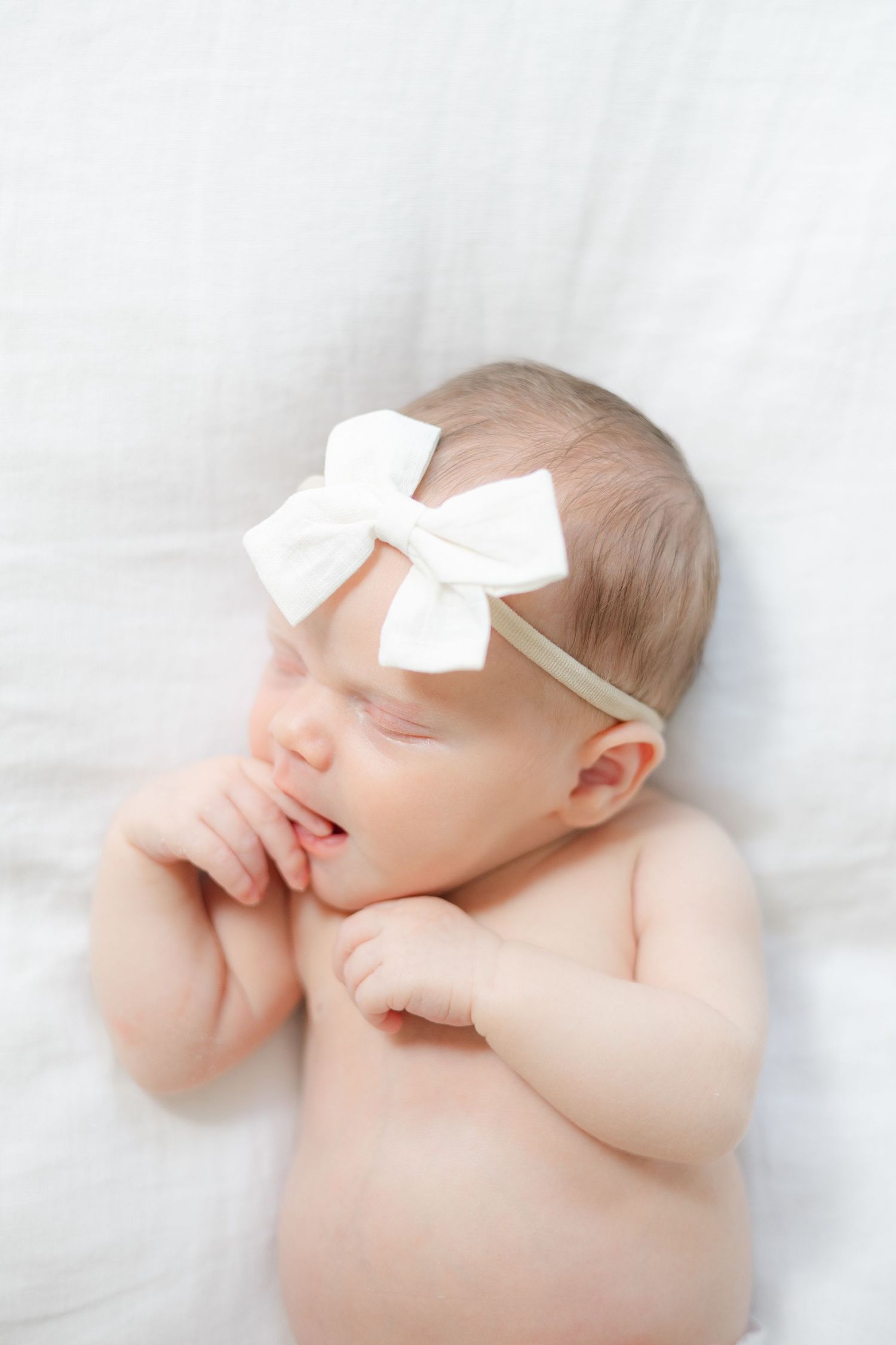Sweet sleeping newborn baby lying on white blanket wearing delicate ivory bow headband.