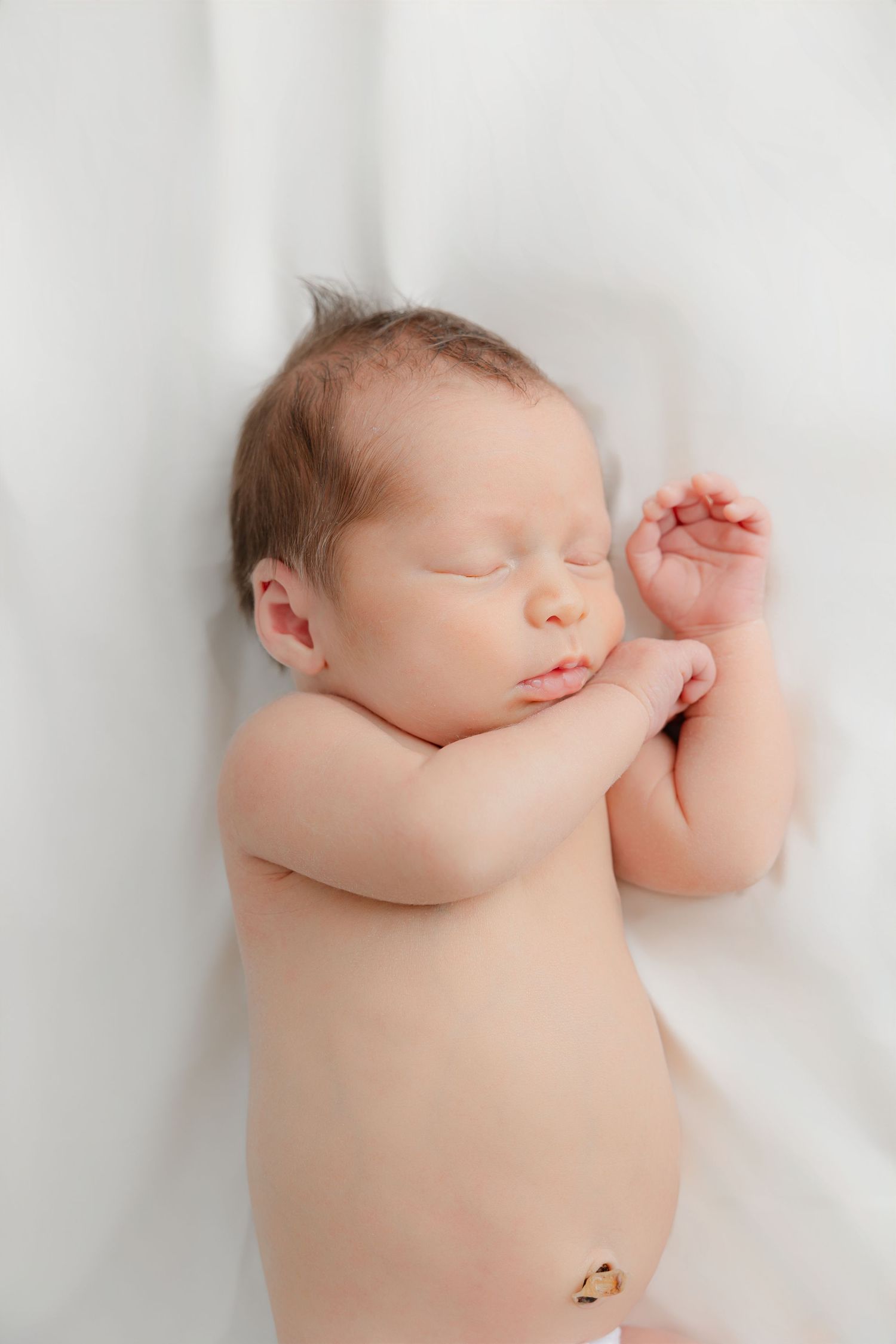 Peaceful newborn baby sleeping on soft white bedding in natural light.