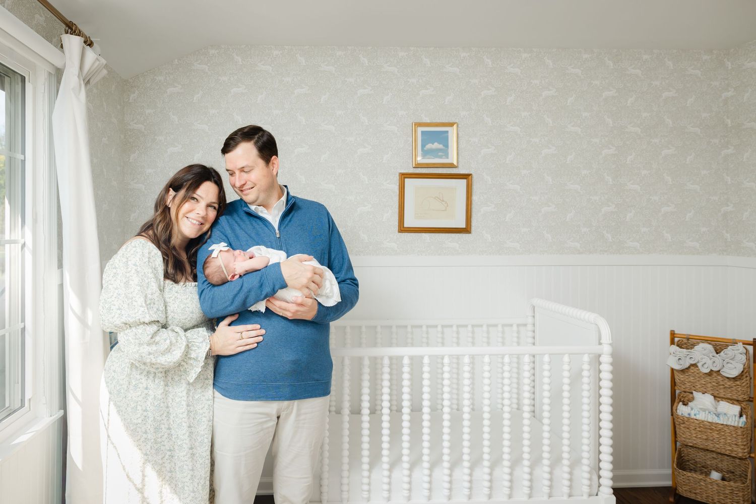 Parents share tender moments with a newborn baby in a nursery decorated with a white crib and natural lighting.