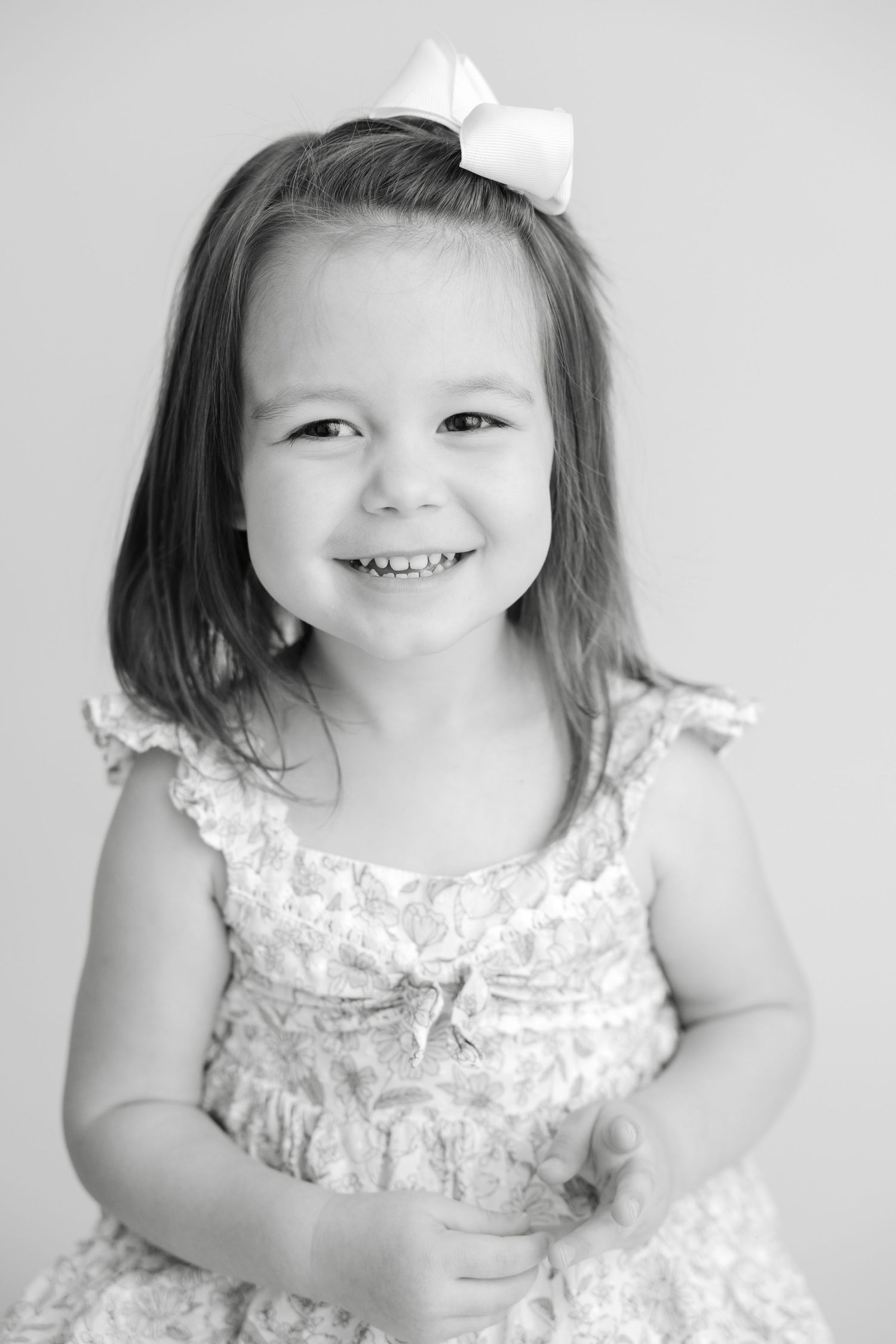 A series of black and white photos showing a young child wearing a white ruffled dress making playful expressions.