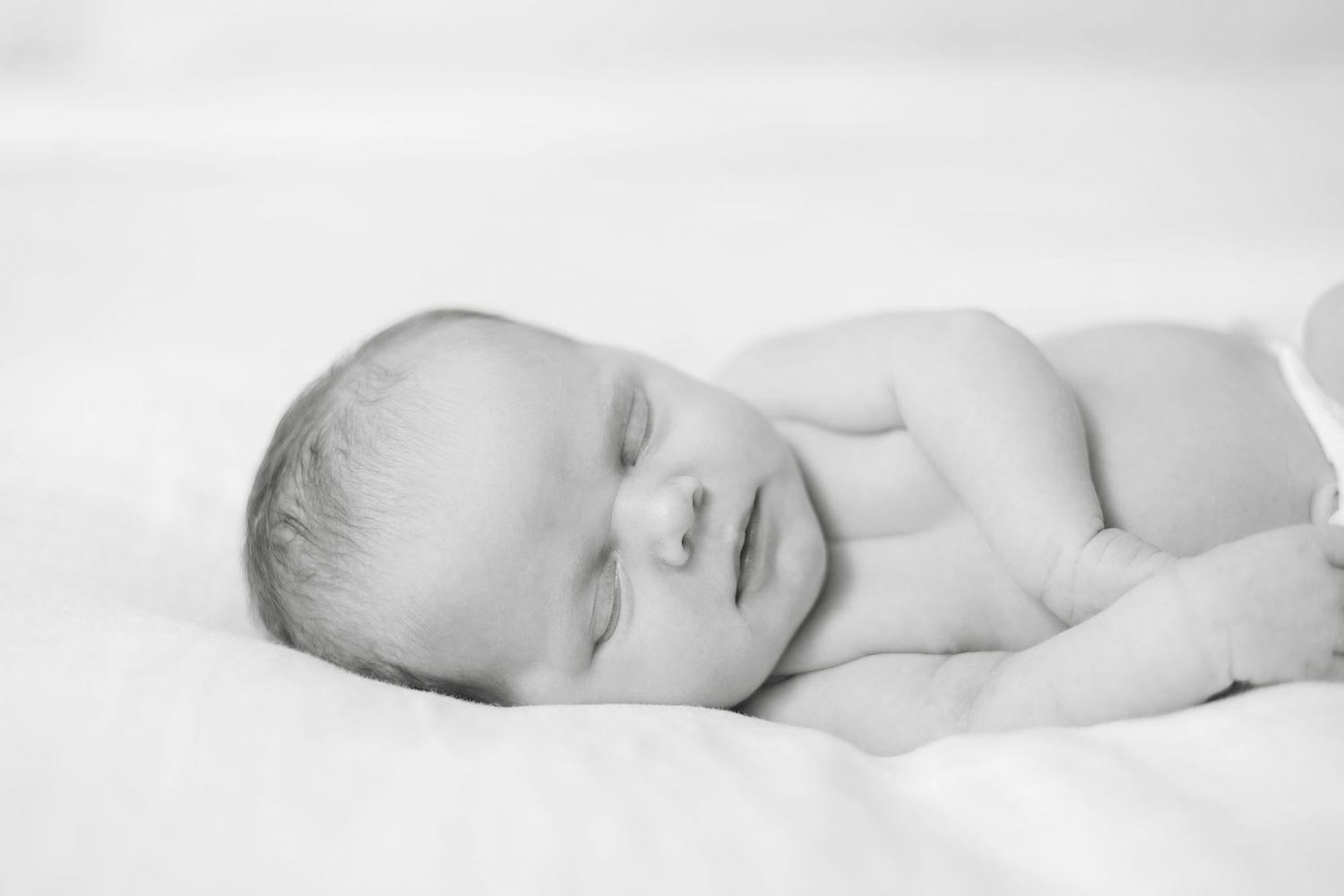 A series of black and white photos showing a sleeping baby in white bedding.