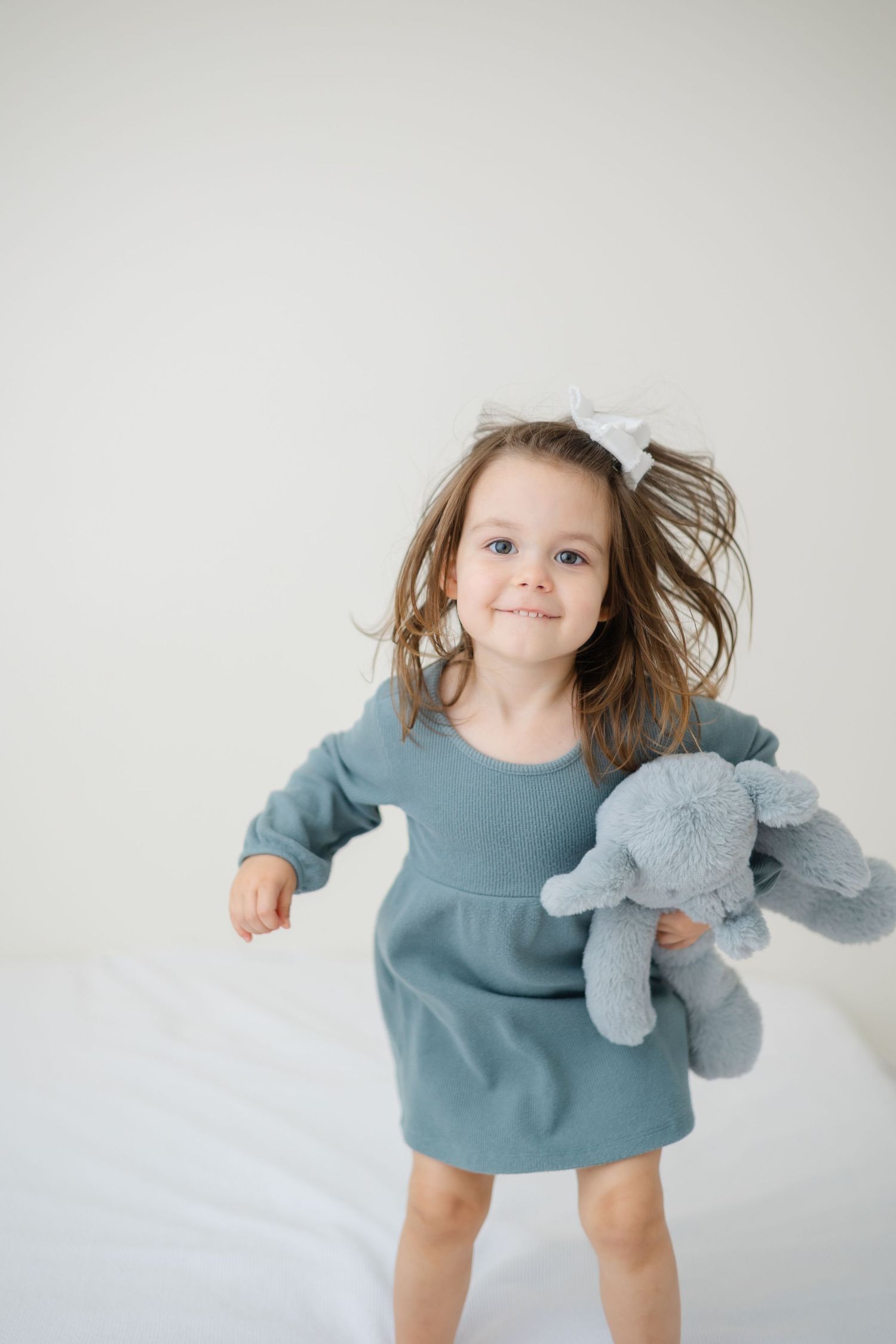 A joyful figure in a blue dress jumps and twirls while holding a plush toy elephant against a white background.