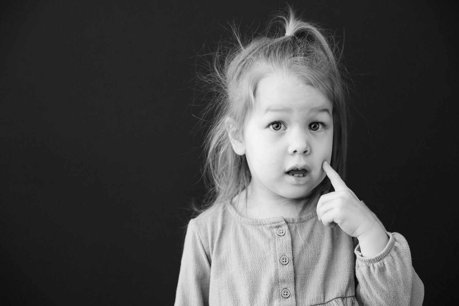 Black and white portrait of a young child with messy hair in a button-up top touching their face.