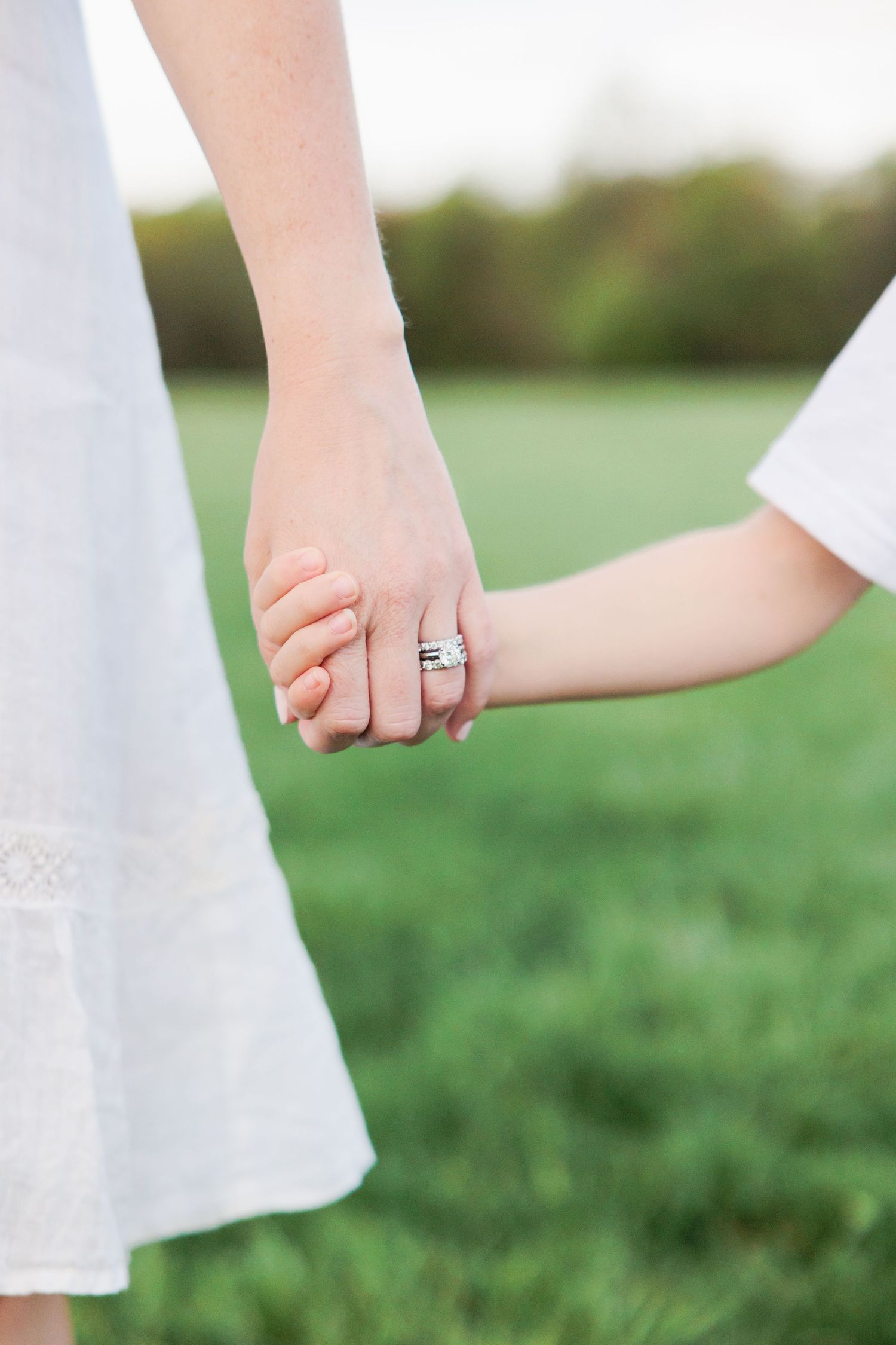 Close-up view of hands holding a delicate white fabric against a soft green grassy background in natural light.
