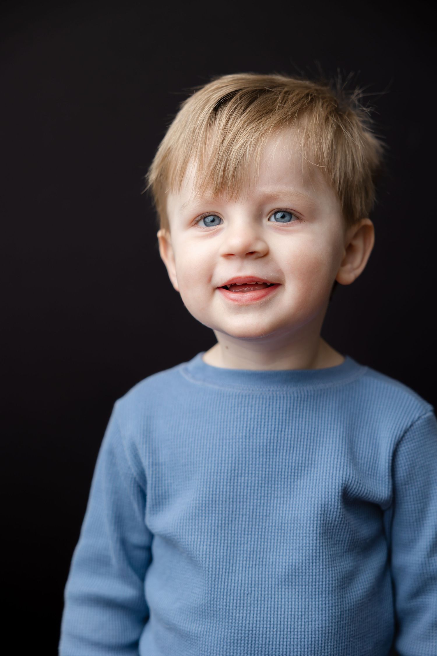 A young child in a light blue sweater poses against a black background in a series of connected portraits.