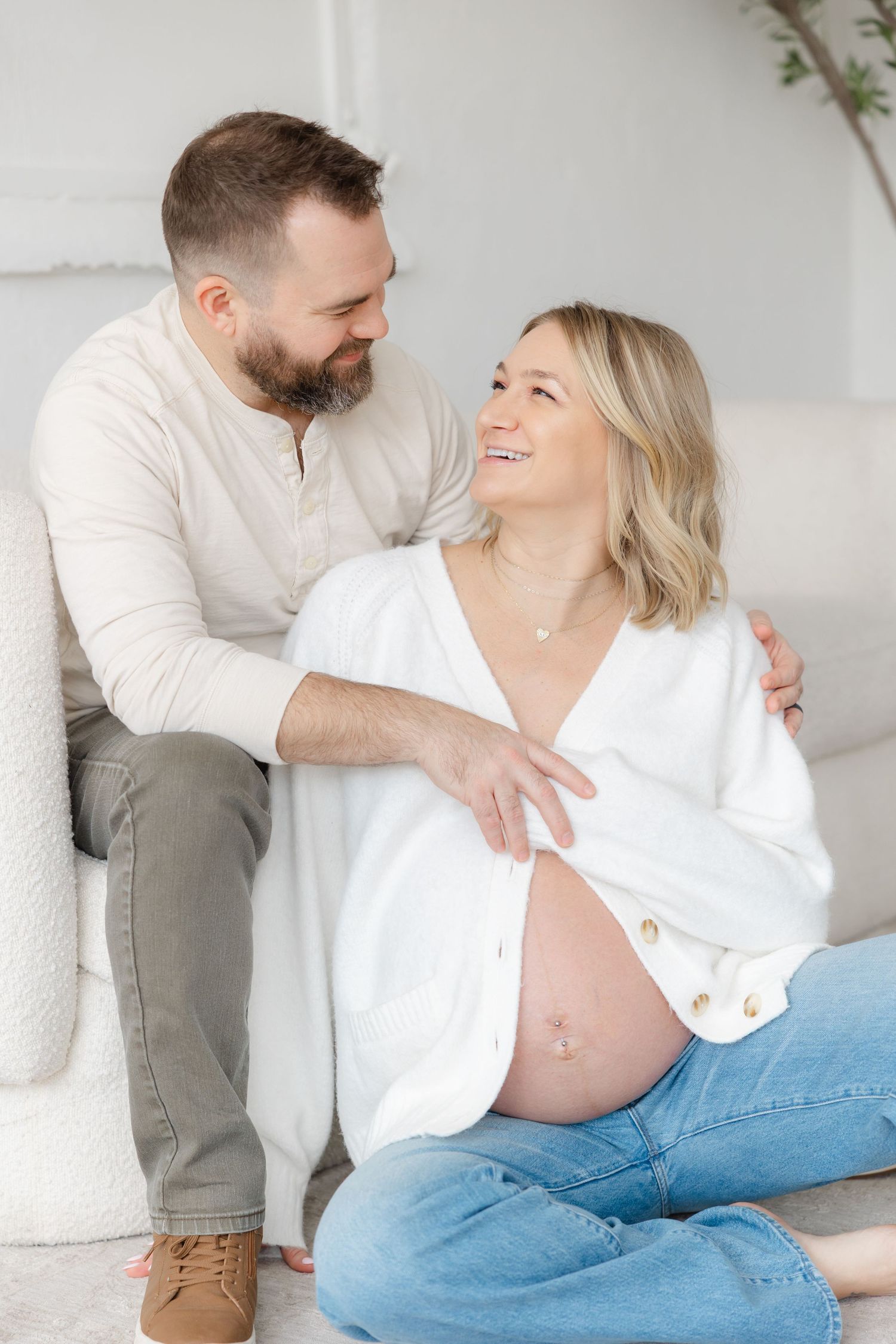 A couple shares a tender moment during a maternity photoshoot, with the pregnant woman wearing a white shirt and jeans.