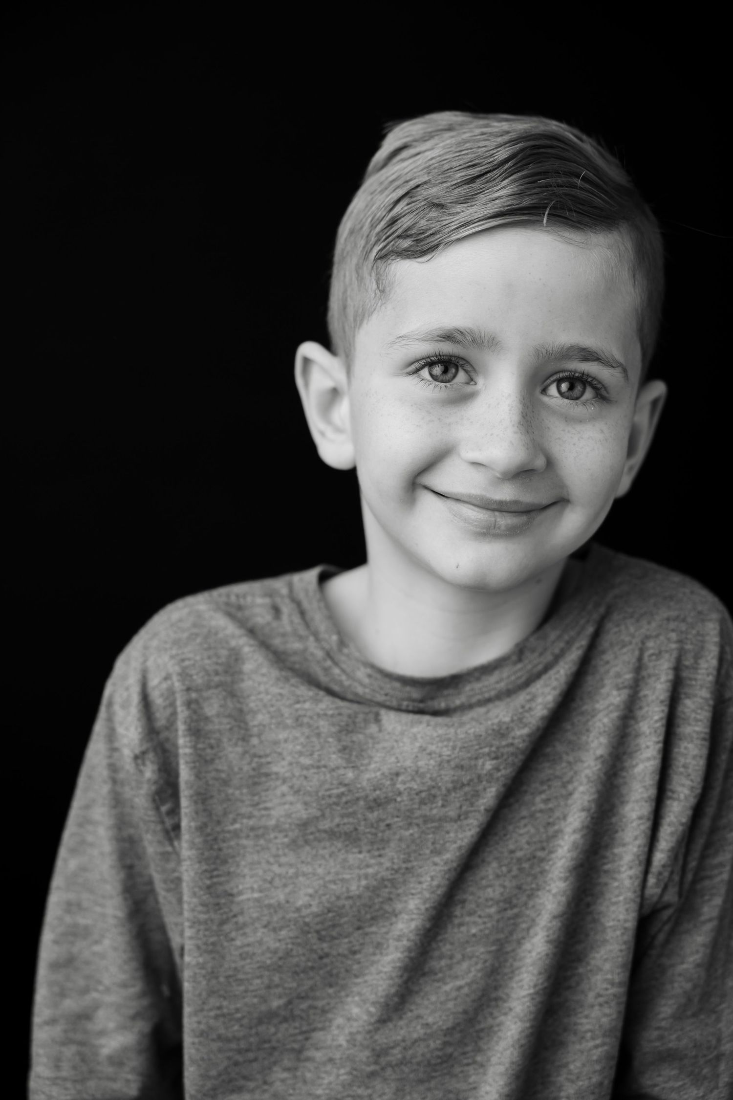 A series of black and white portraits showing a child in a gray sweater with various playful expressions.