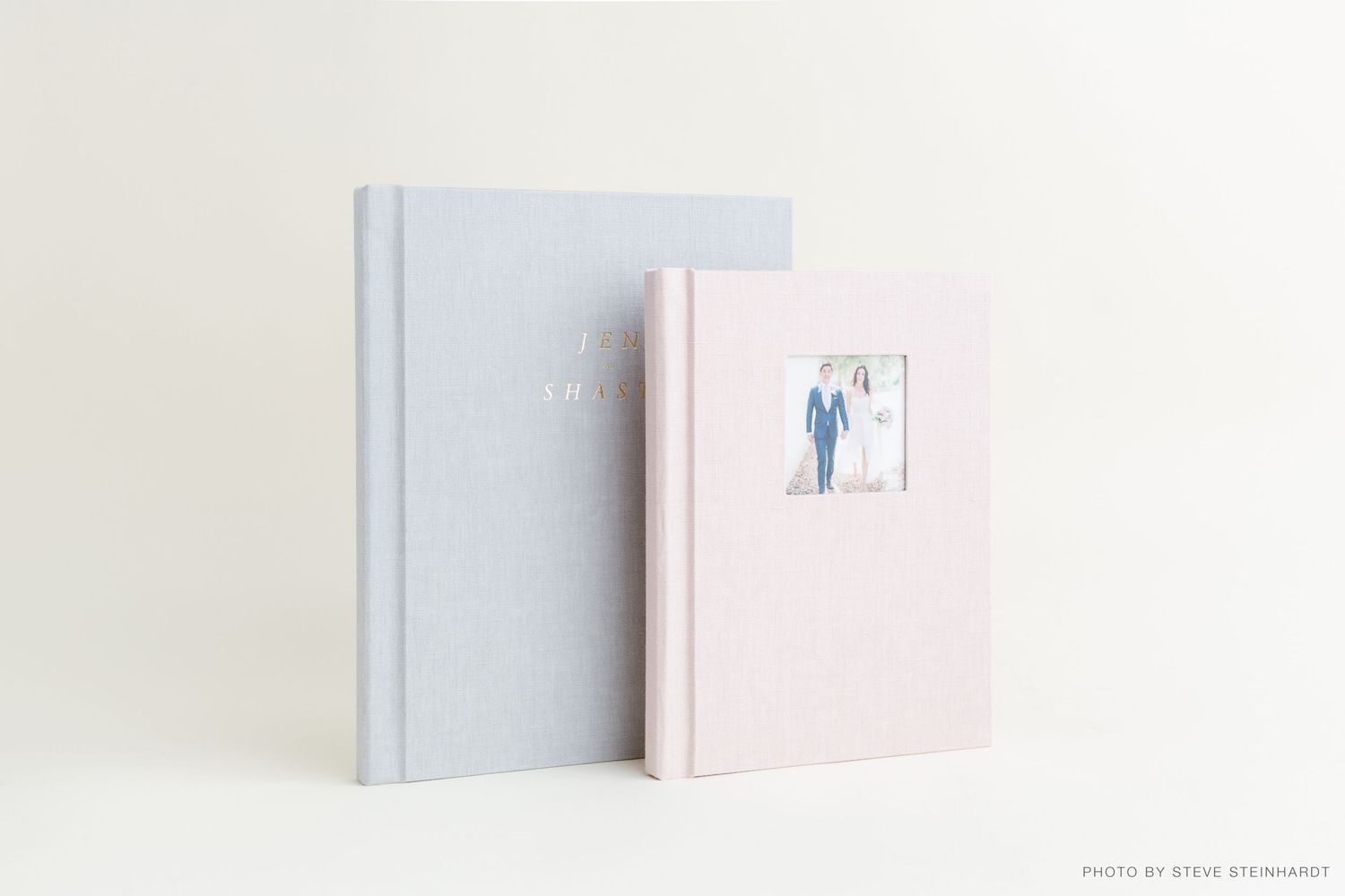 Minimalist white wall display with pastel pink and gray books arranged on floating shelves.