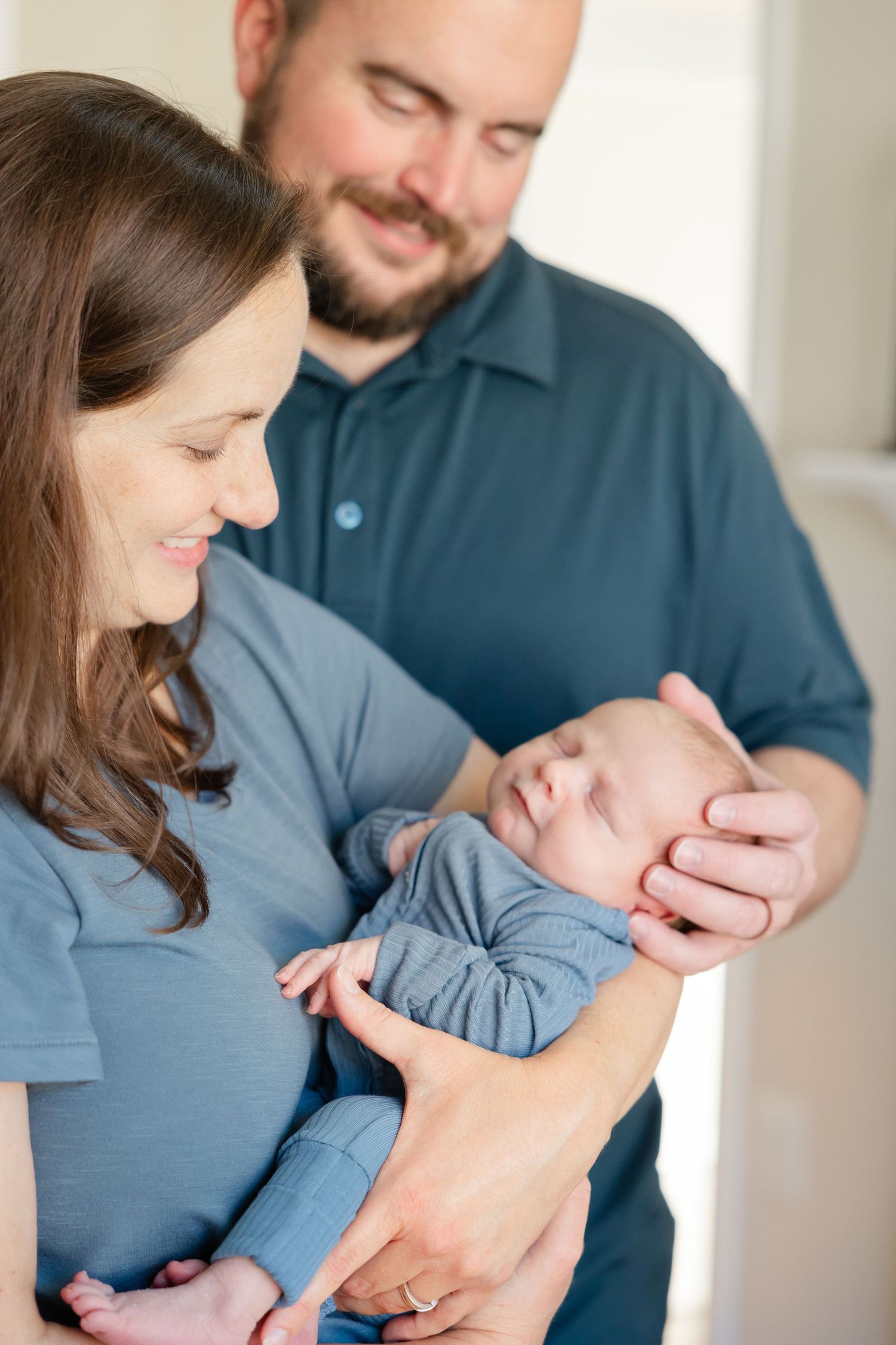 Parents tenderly holding their sleeping newborn baby dressed in soft blue clothing.