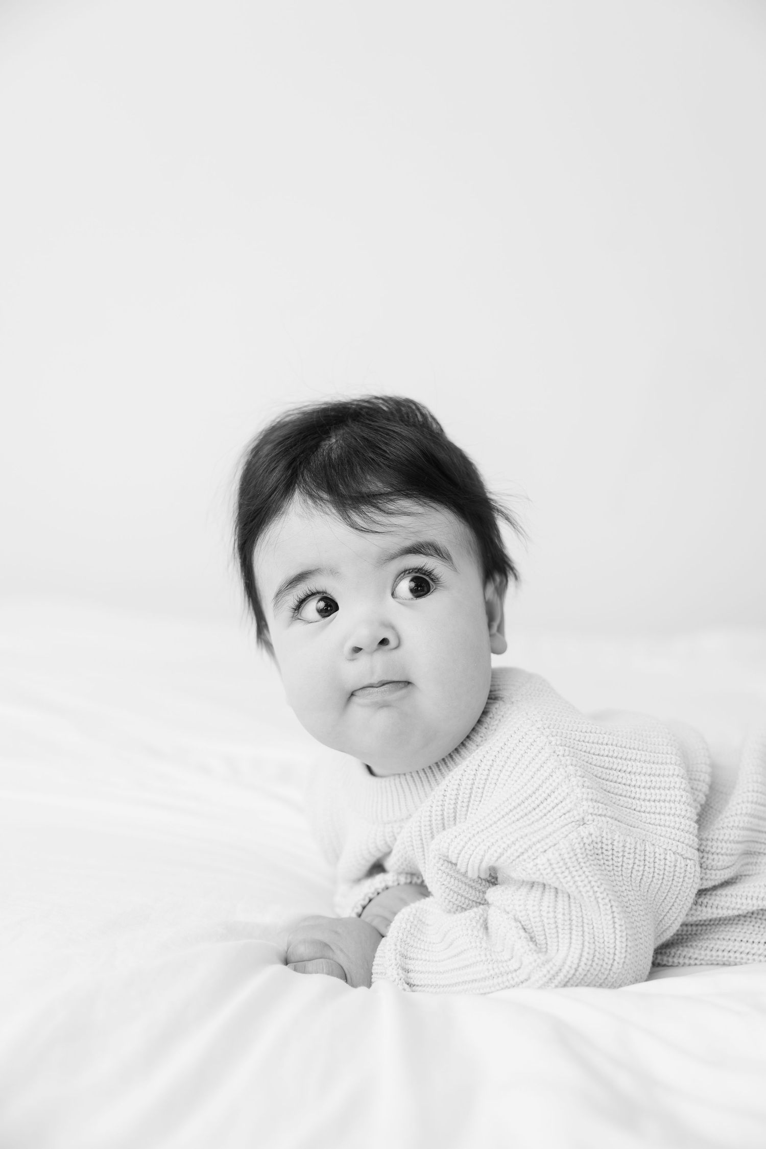 Black and white portrait series of a baby lying on white bedding looking upward with curious expressions.