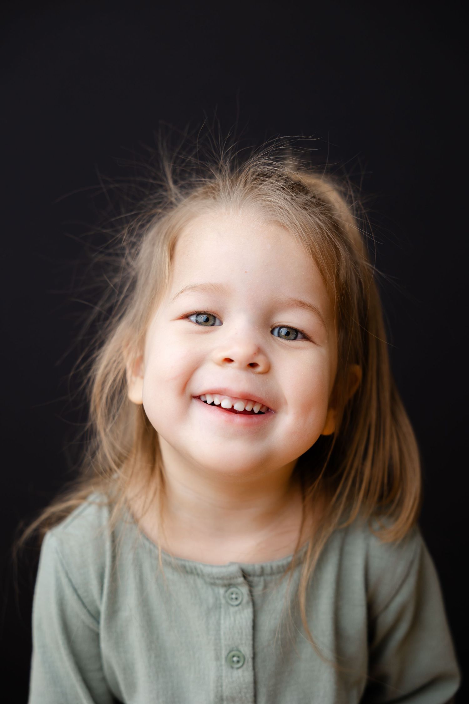 A series of moody portrait shots against black background shows a small child's smiling expressions in a gray sweater.