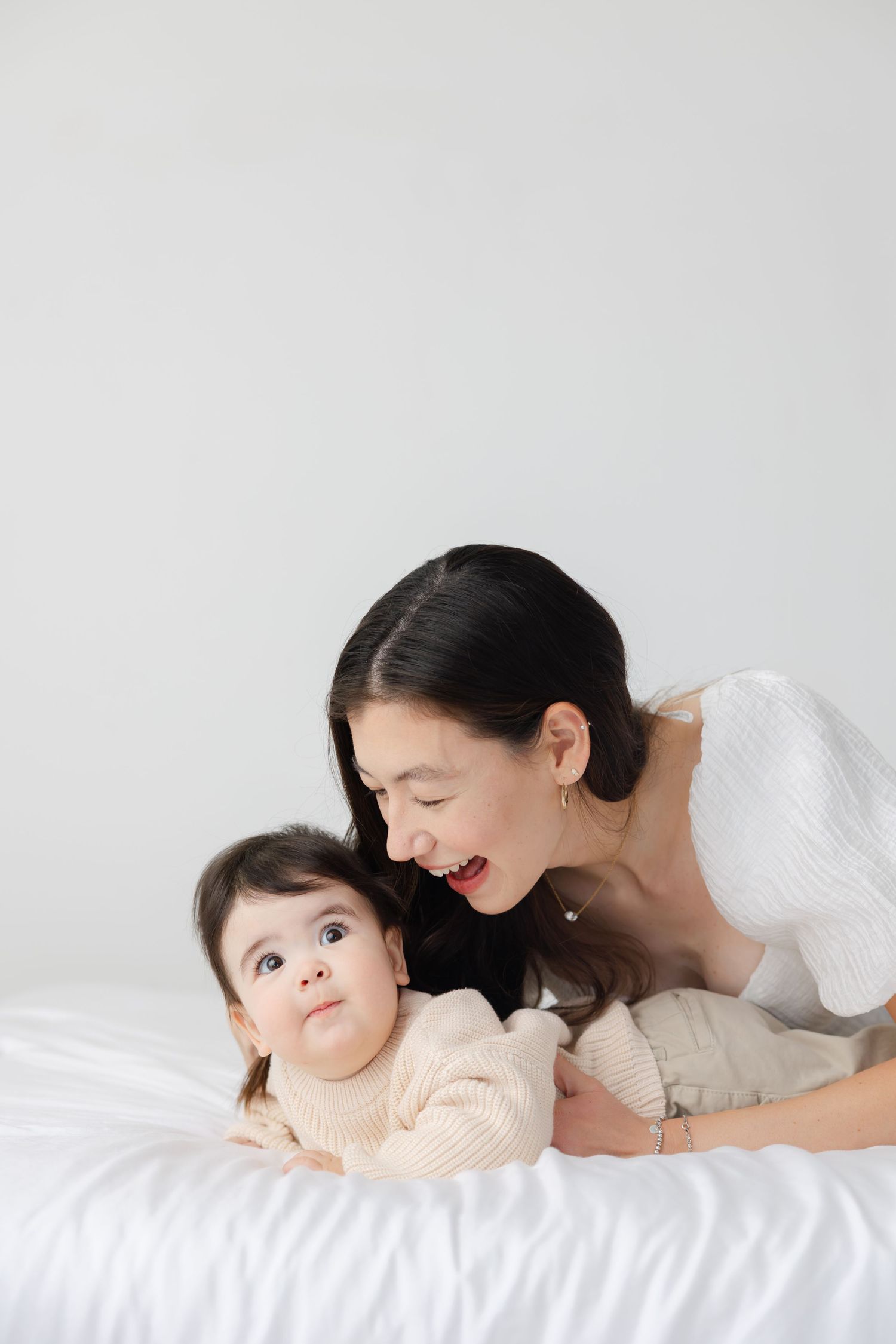 A tender moment between parent and baby lying together on white bedding in a series of connected photos.