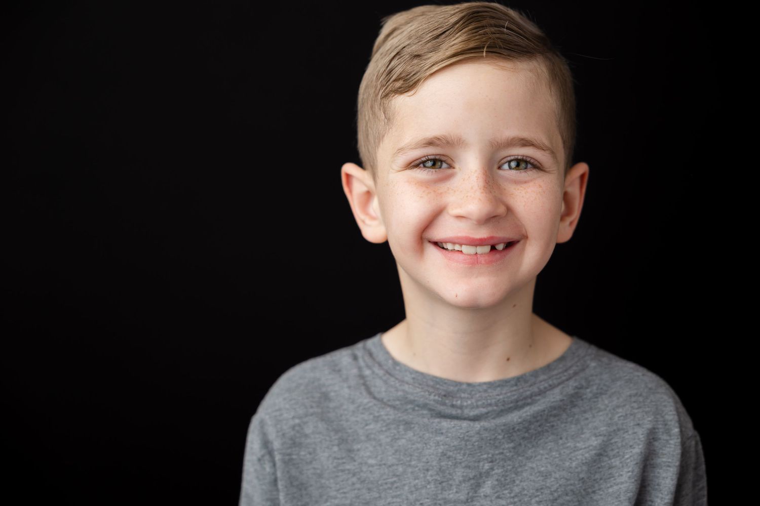 Young person in a gray t-shirt smiling at the camera against a dark background.