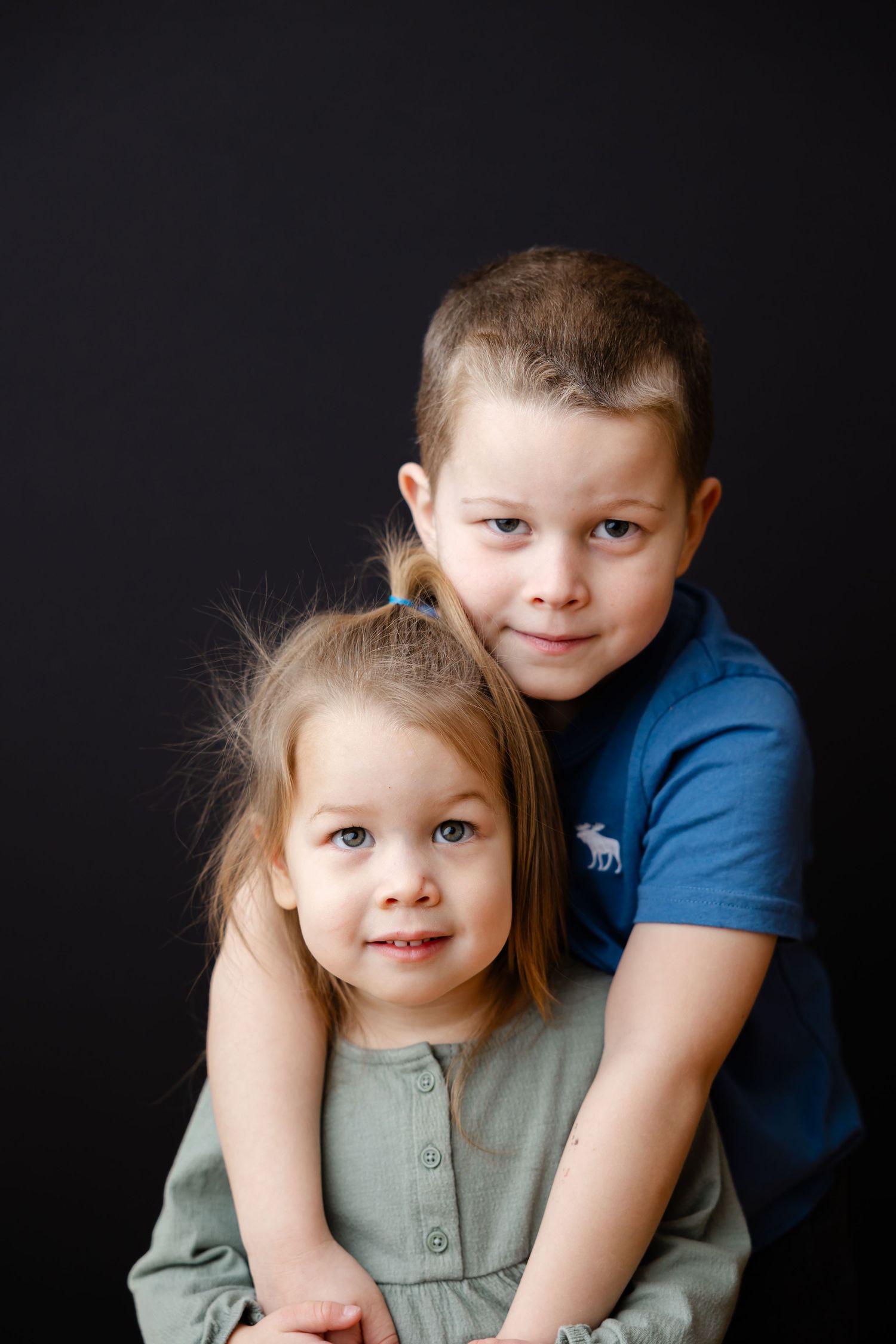 Portrait of two young siblings in casual clothing against a dark background.