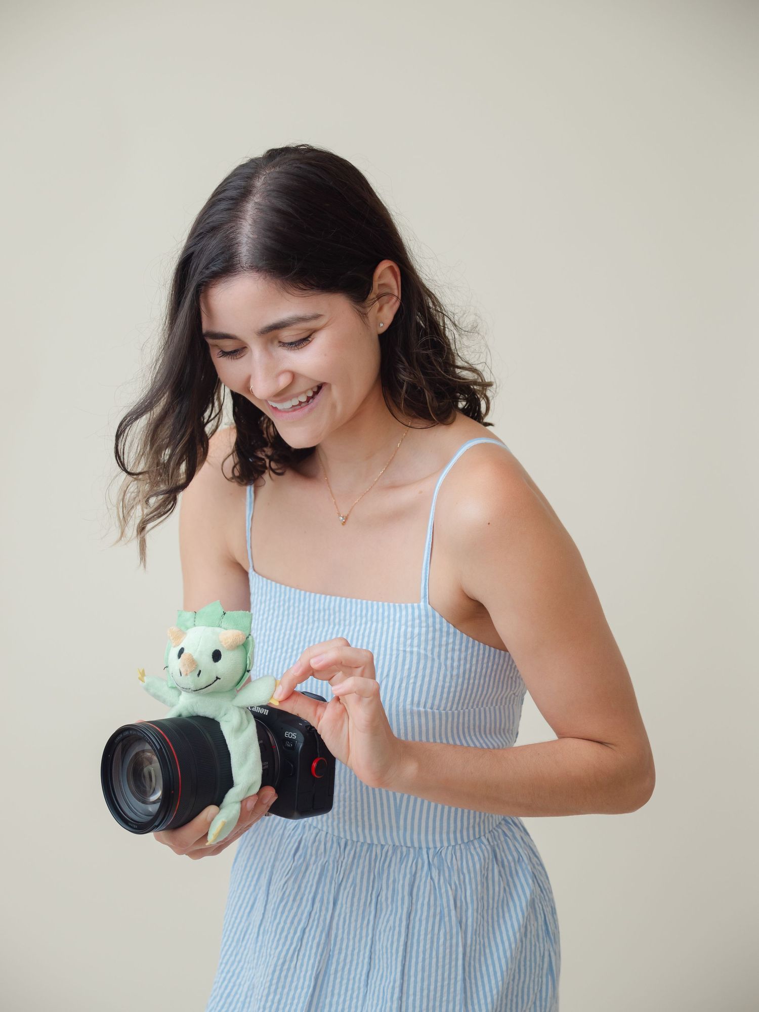 A person in a blue striped dress laughs while holding and cleaning a camera lens with a microfiber cloth.