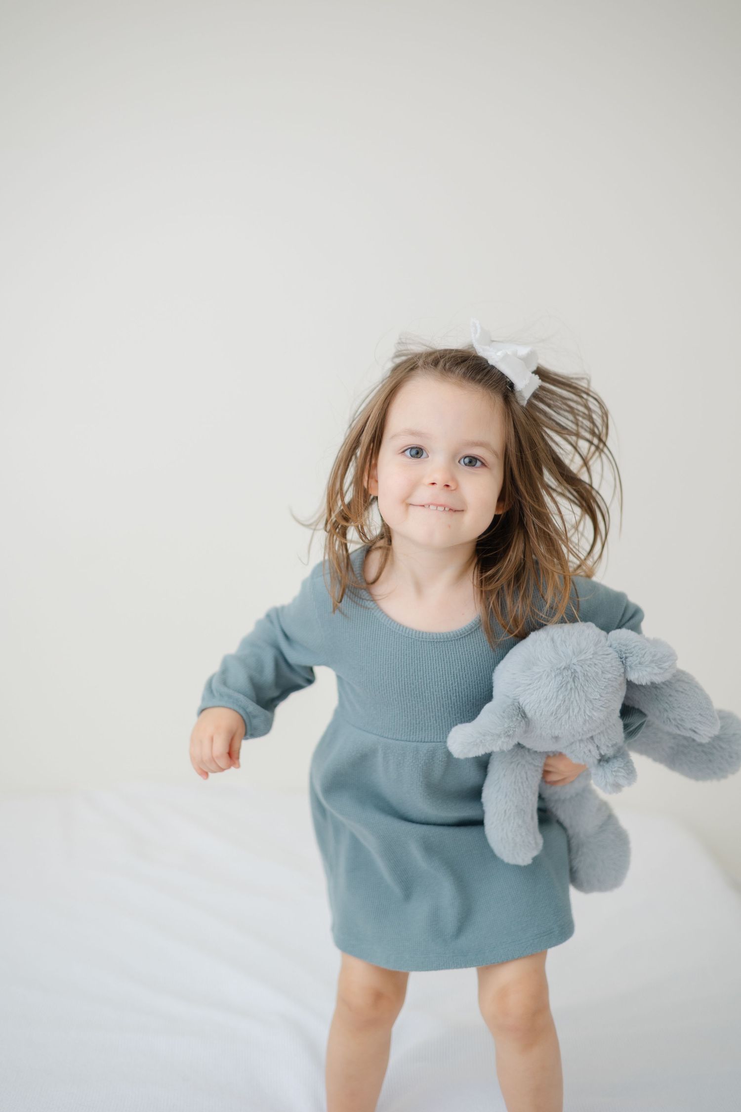 A photo of an energetic toddler girl jumping on a bed taken during an in-home studio style session with Hello Indy Photography.