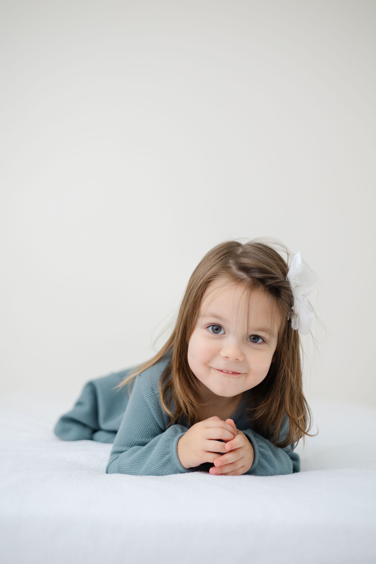 A sweet portrait series of a child in a blue sweater lying on white bedding showing different playful expressions.