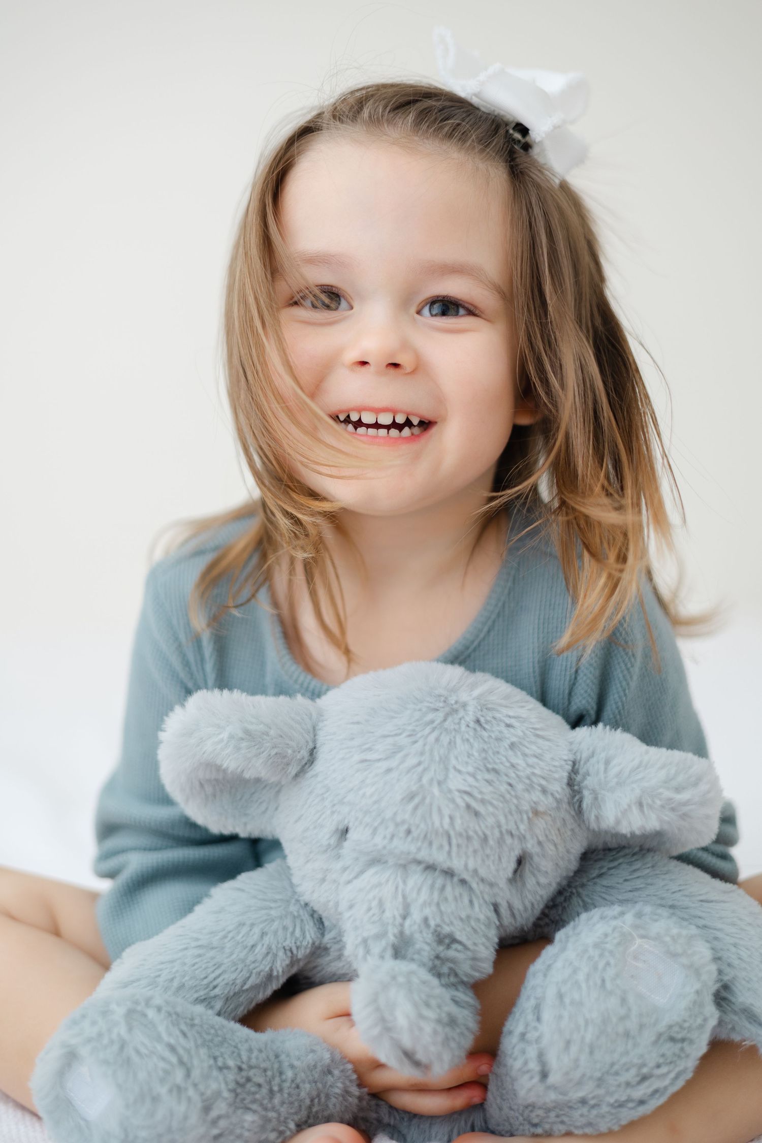 Child in blue sweater hugs soft gray plush toy elephant against white background.