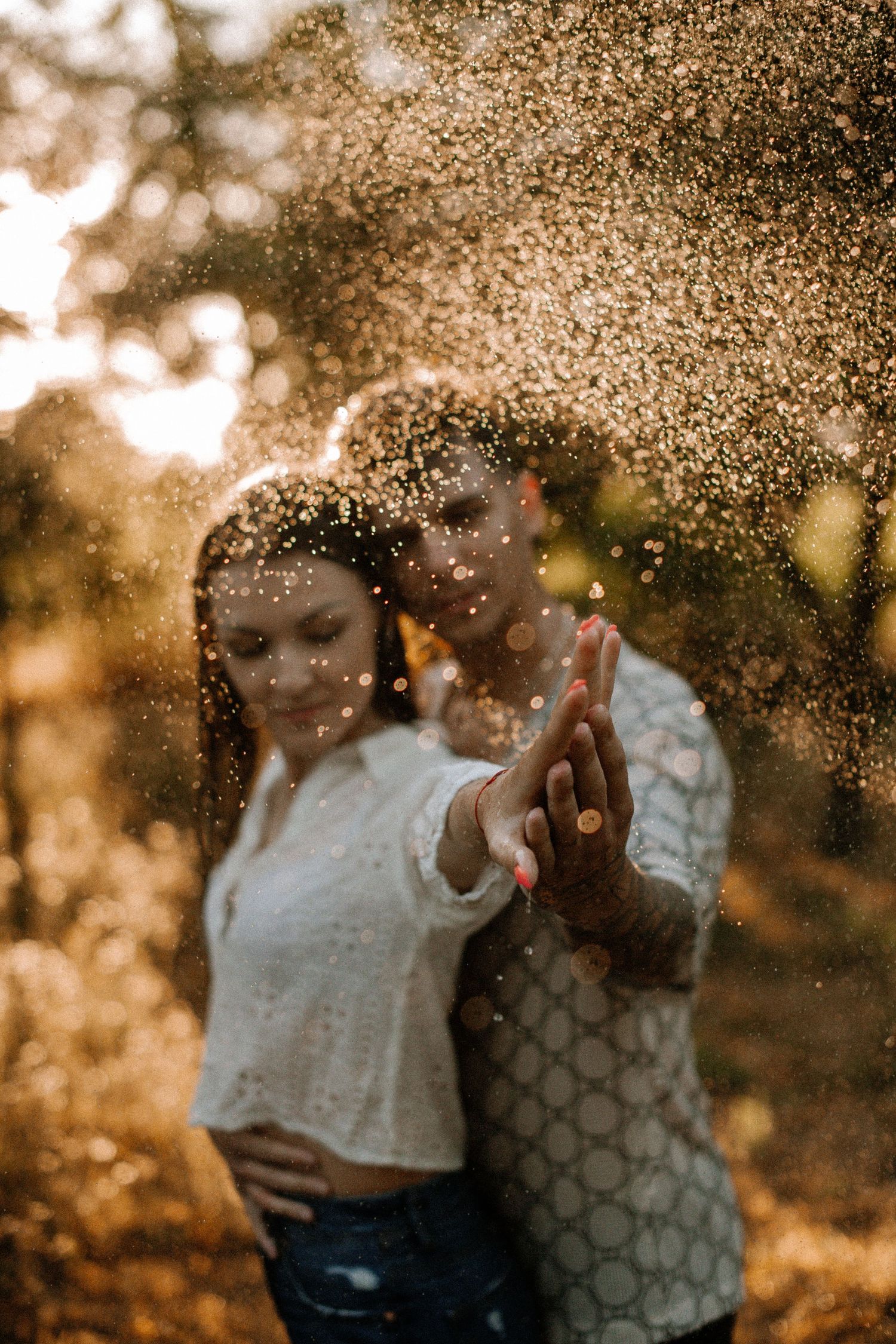 Artistic portrait in golden sunlight with water droplets creating sparkle effect.