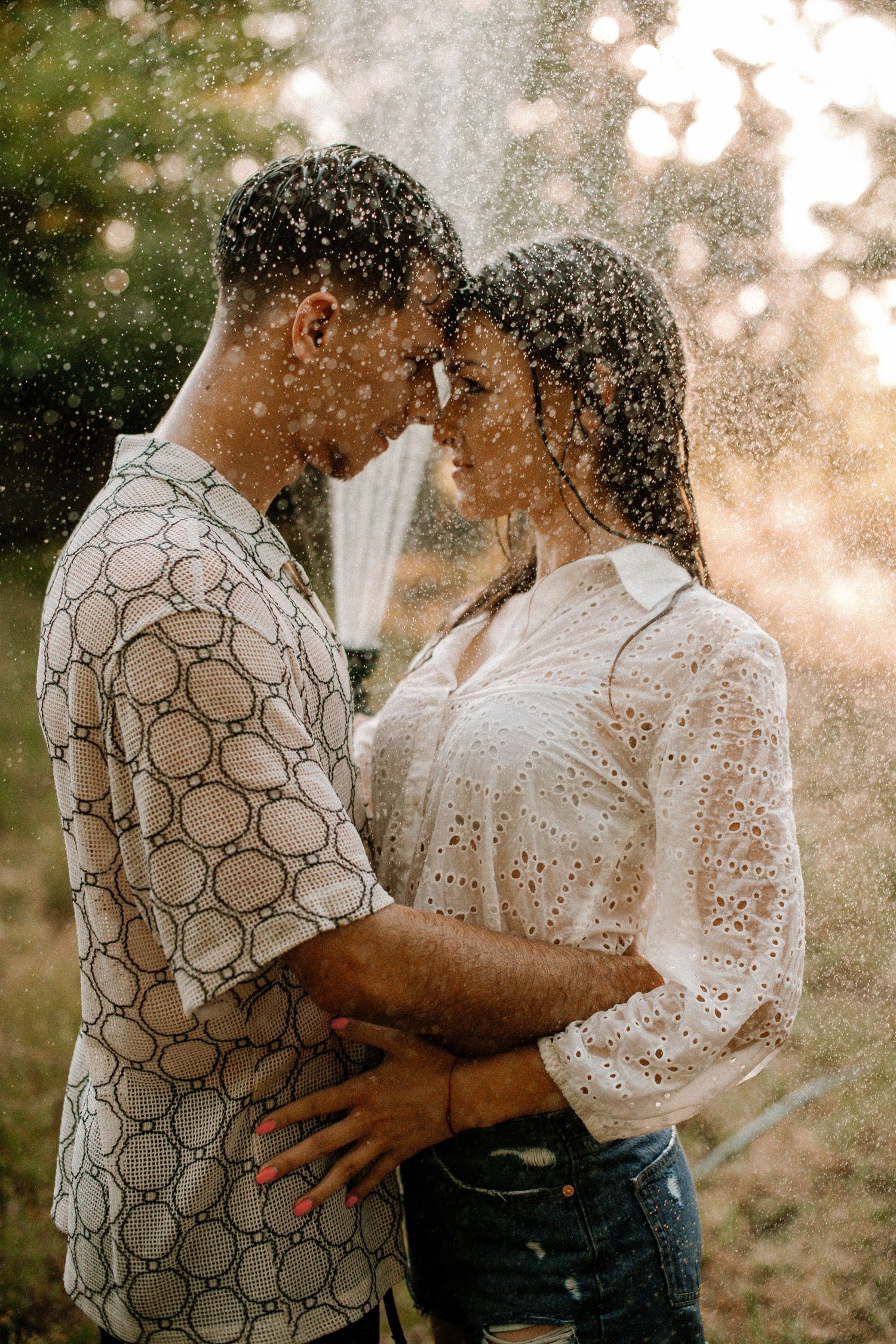 Romantic couple sharing intimate moment in sunlit water spray.