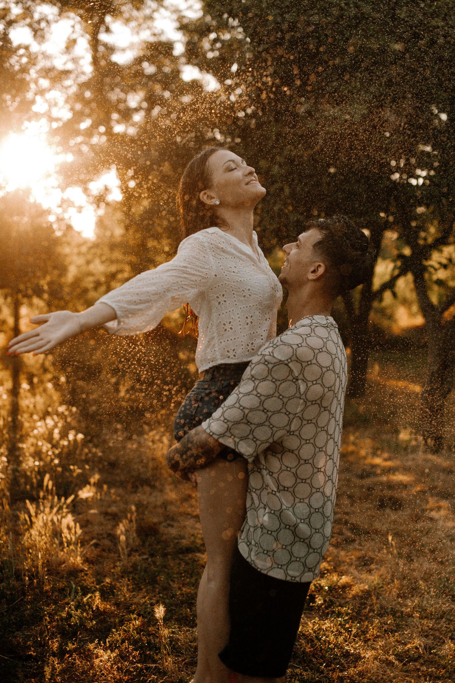 Joyful lift pose in golden sunset with water spray effect.