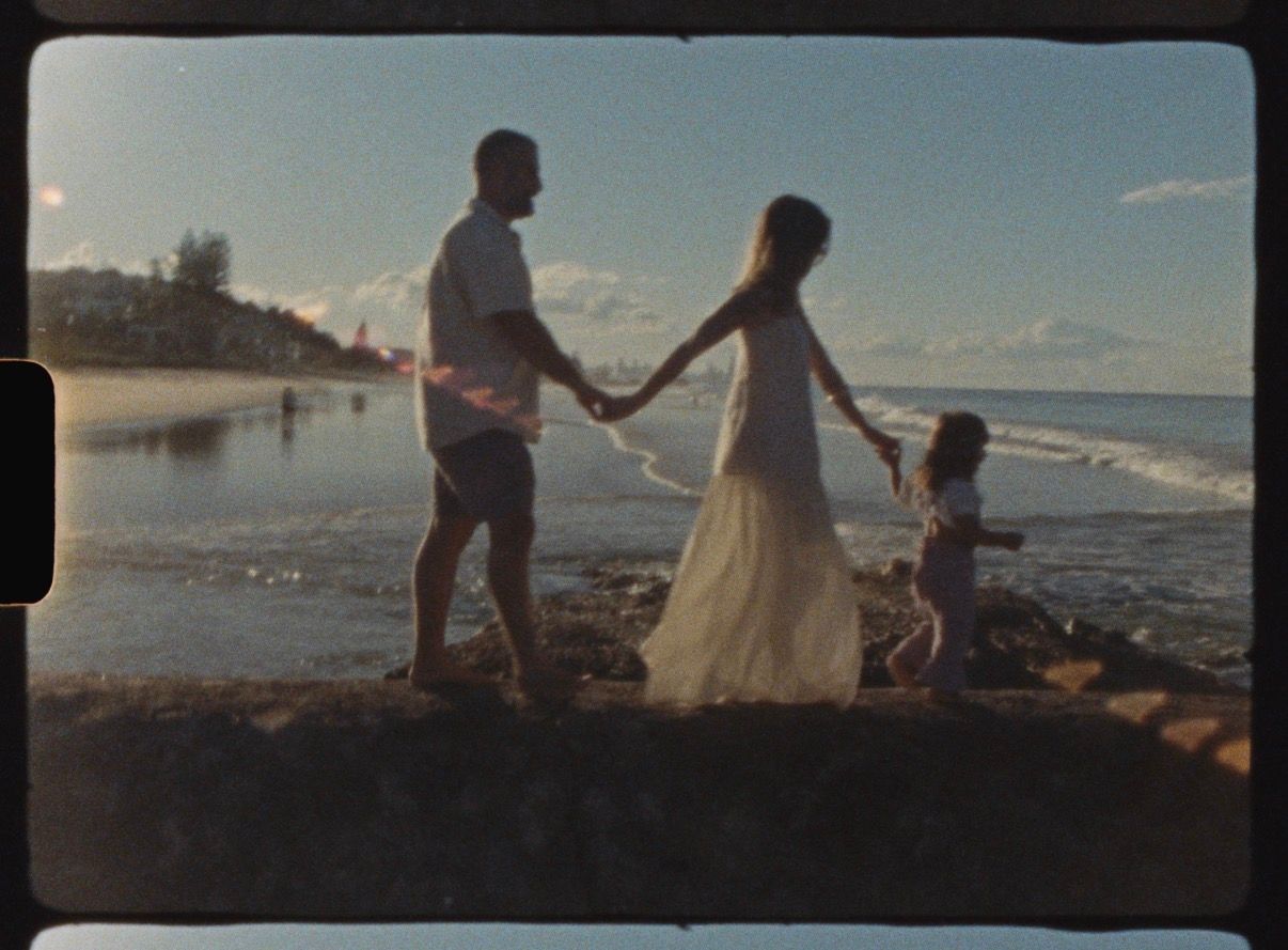 Parents walking hand in hand with their daughter during a Super 8 family film session at Currumbin Beach.