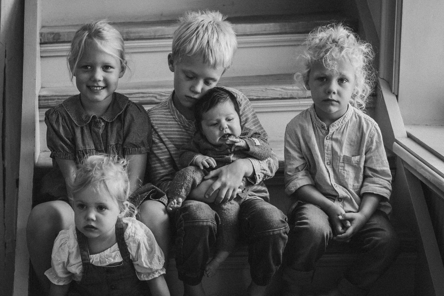 Svartvit bild på fem syskon som sitter i en trappa med sin nyfödda lillasyster.