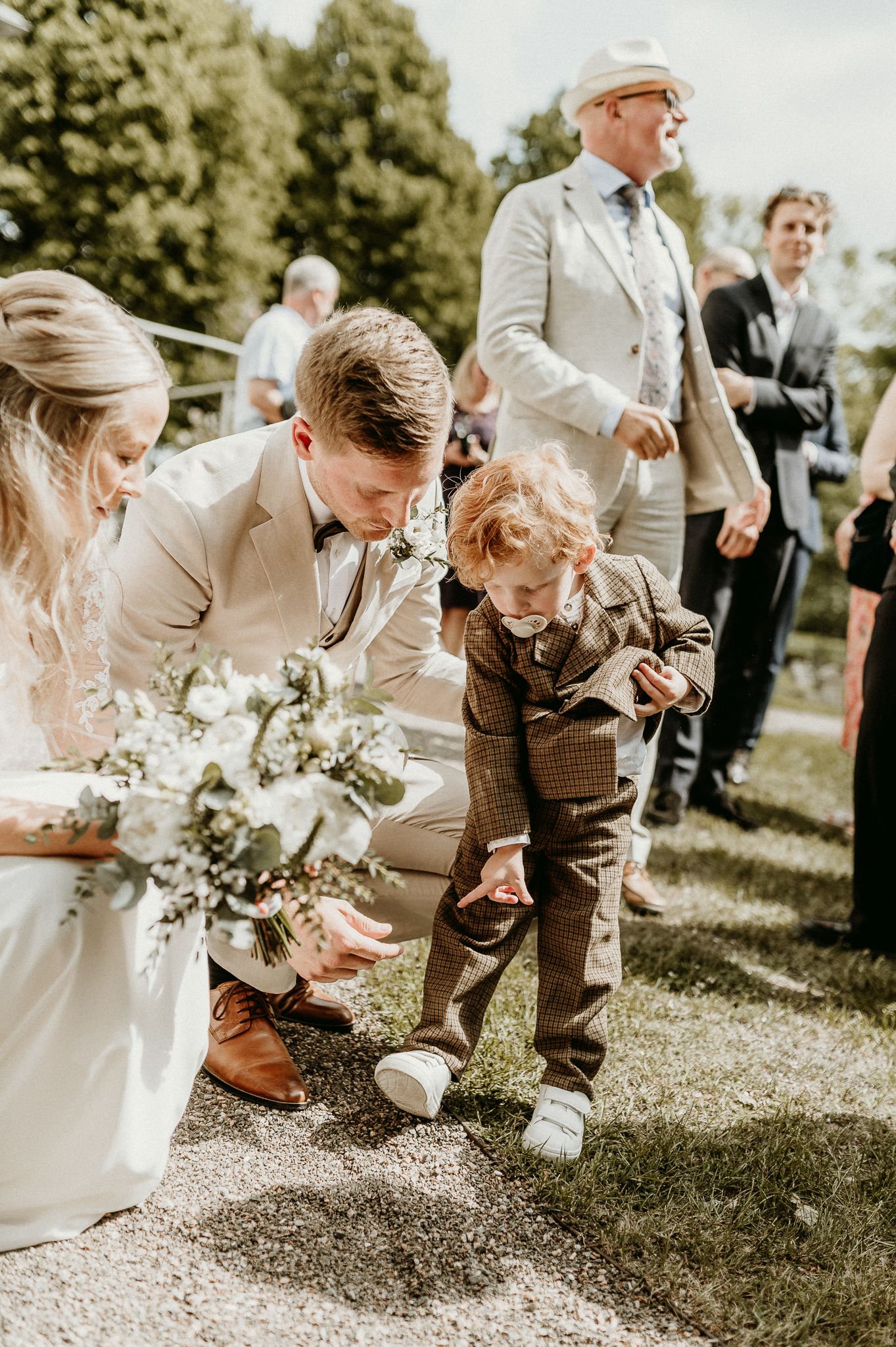 Liten pojke med napp i munnen, pekar på sina nya skor och visar dom för ett brudpar som nyss gratulerats på trappan till en kyrka i Örebro.