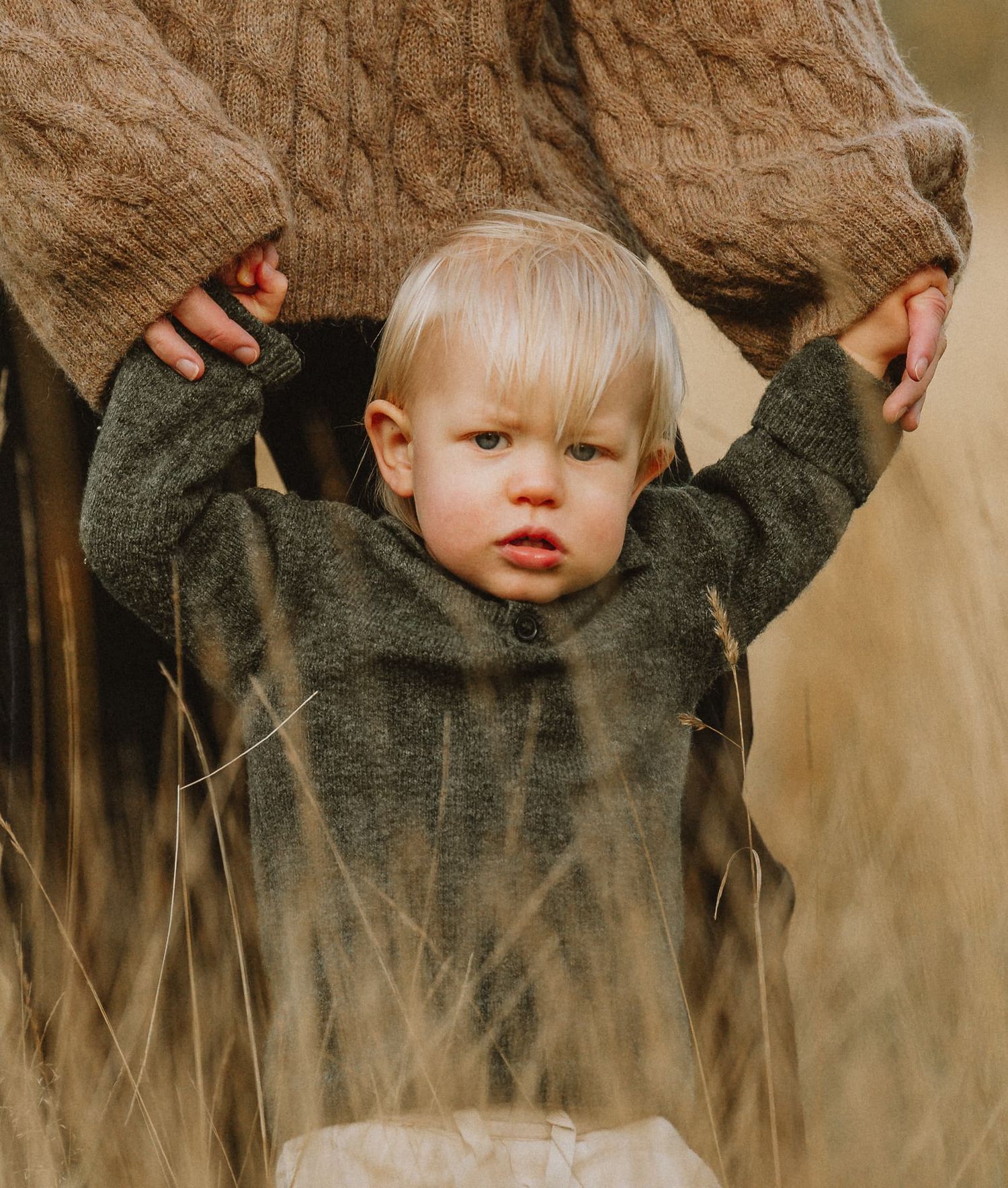 Pojke håller sin mamma i händerna och går i det höga gyllengula gräset, under en familjefotografering vid Näs Herrgård, Mullsjö/Jönköping.
