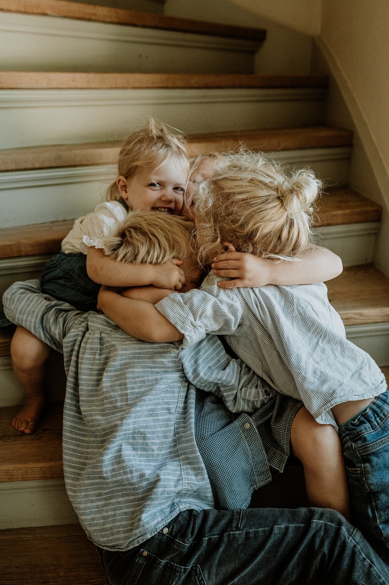 Fem barn sitter i en trappa i sitt gamla hus och kramas. Barnen har kläder i blå toner.
